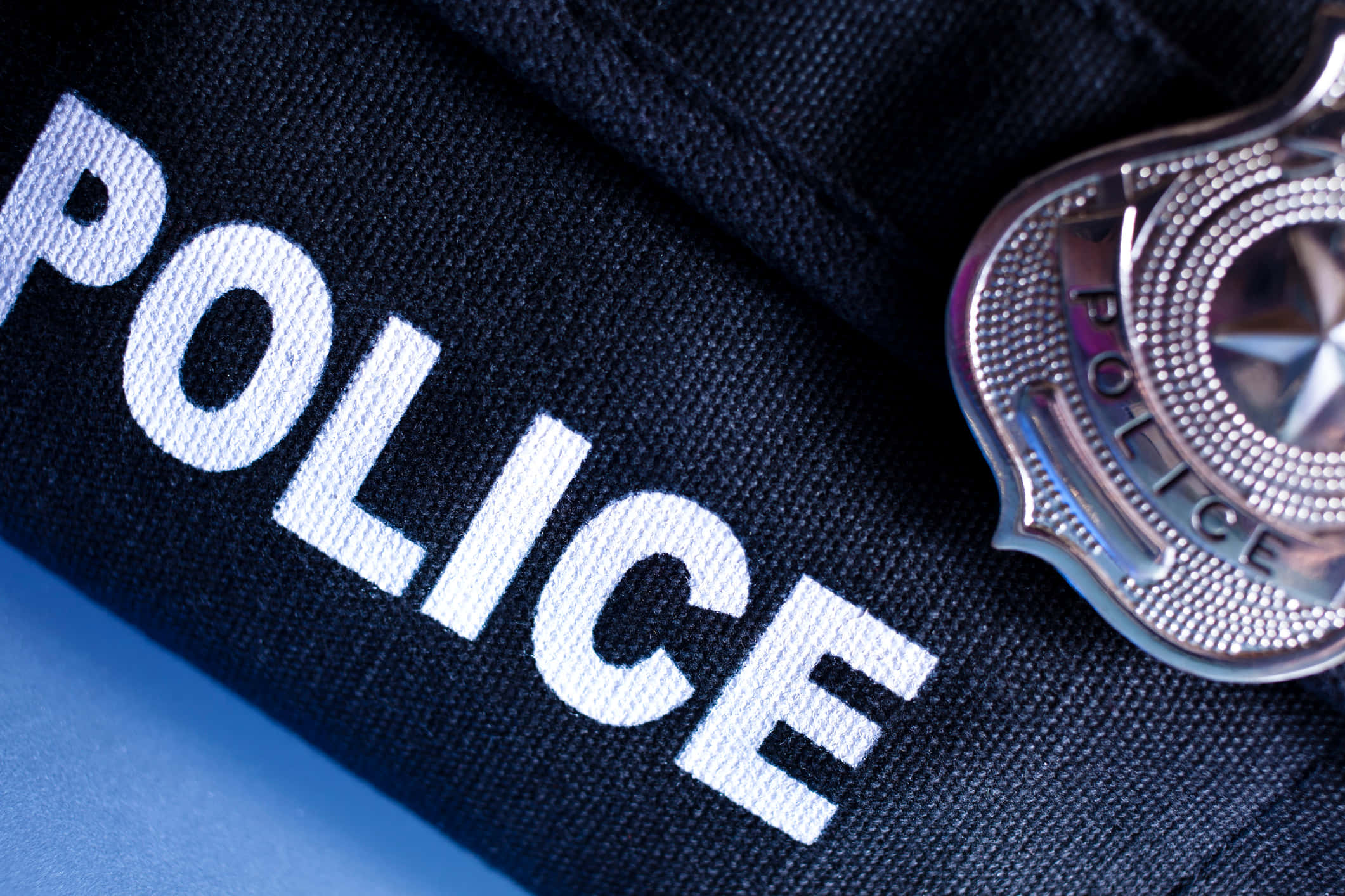 Law Enforcement 桌布 壁紙 — 閃亮警察徽章的特寫，放在深藍色警察制服布料上，帶有白色刺繡文字。