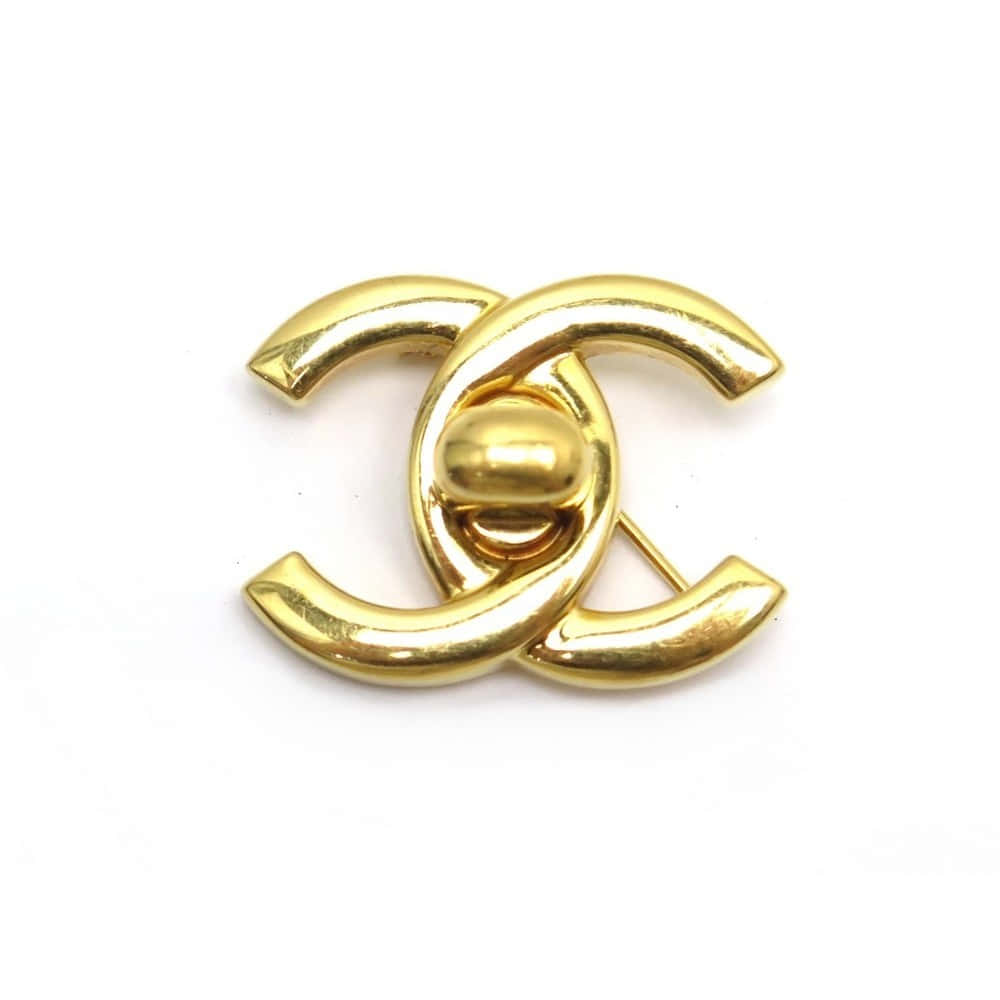 香奈兒標誌 桌布 壁紙 — 閃亮金色Chanel CC標誌胸針，帶有交織的C字和中央珠子，置於純白背景上。