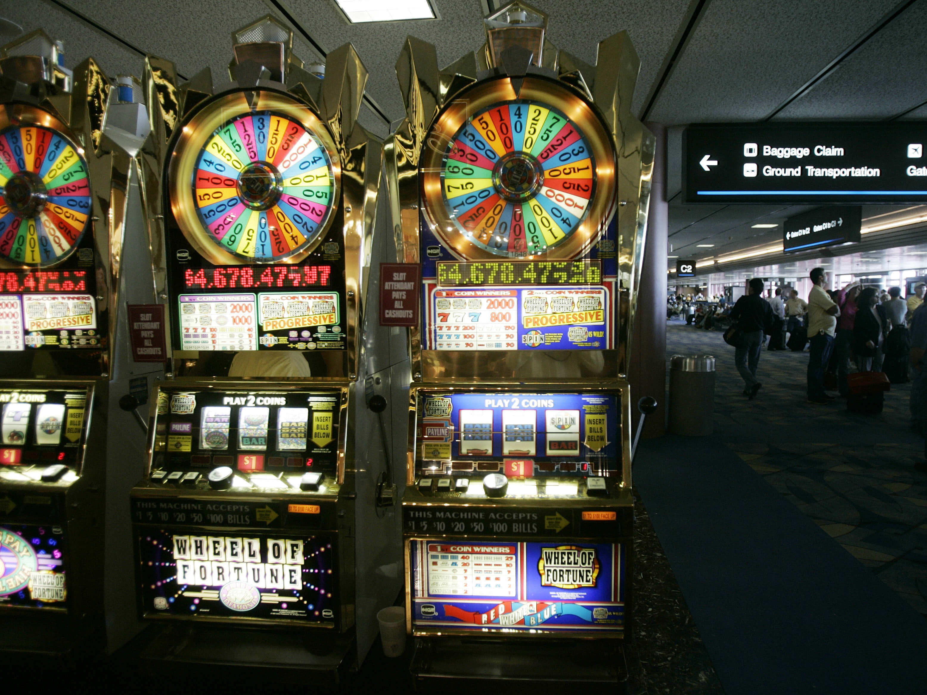 Slot Machine 桌布 壁紙 — 閃亮金色的 Wheel of Fortune 老虎機在繁忙的機場航廈中明亮發光，旅客們走過。