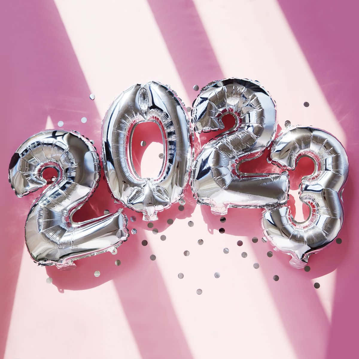 New Year 桌布 壁紙 — 閃亮銀色2023數字氣球放置在粉紅色表面上，周圍散落著五彩紙屑和戲劇性的光線。