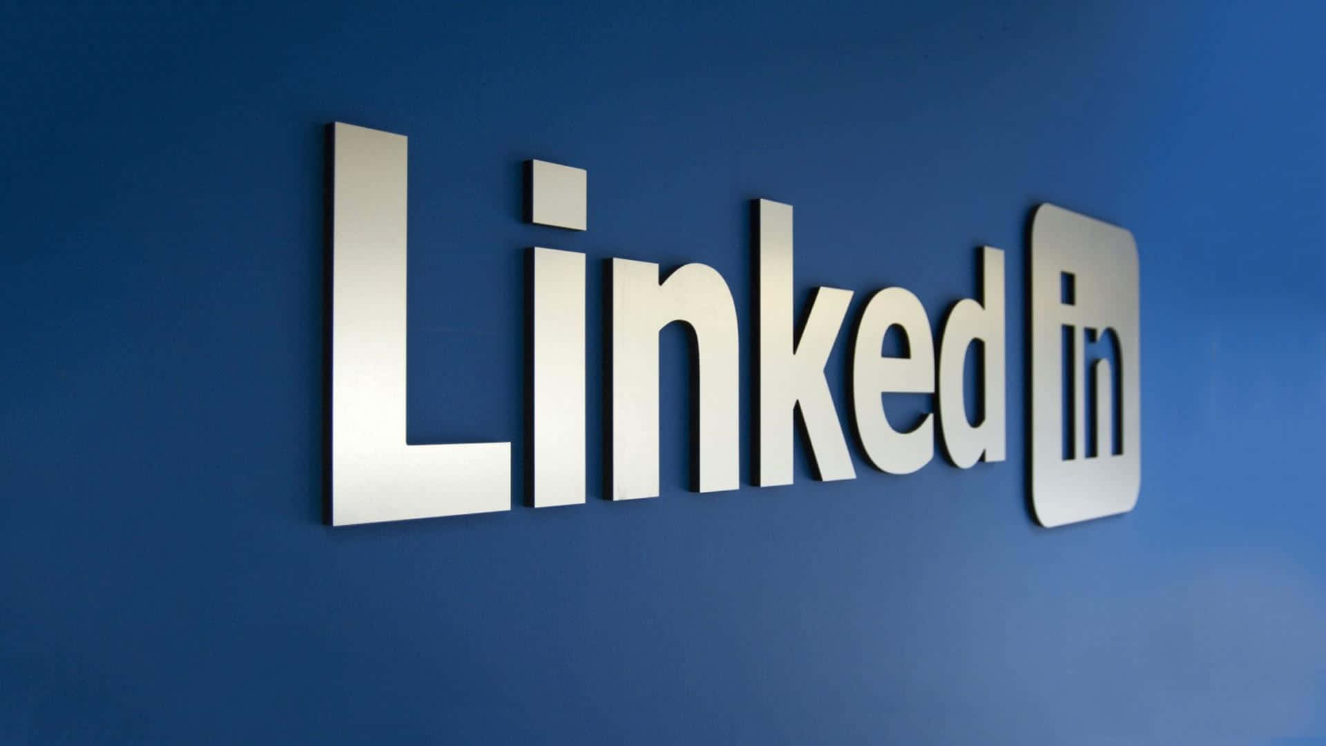 Linkedin Logo 桌布 壁紙 — 閃亮銀色LinkedIn標誌安裝在現代辦公室環境的深藍色牆上。