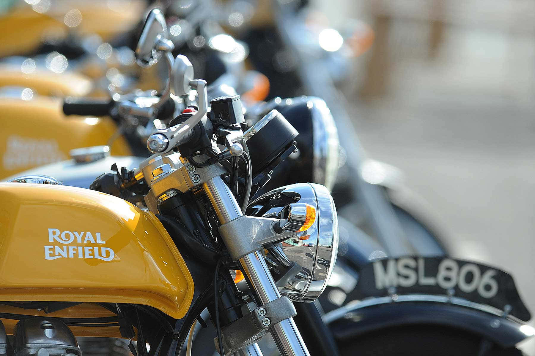  壁紙 — 閃亮黃色 Royal Enfield 摩托車的特寫，帶有鍍鉻細節和模糊的背景摩托車。