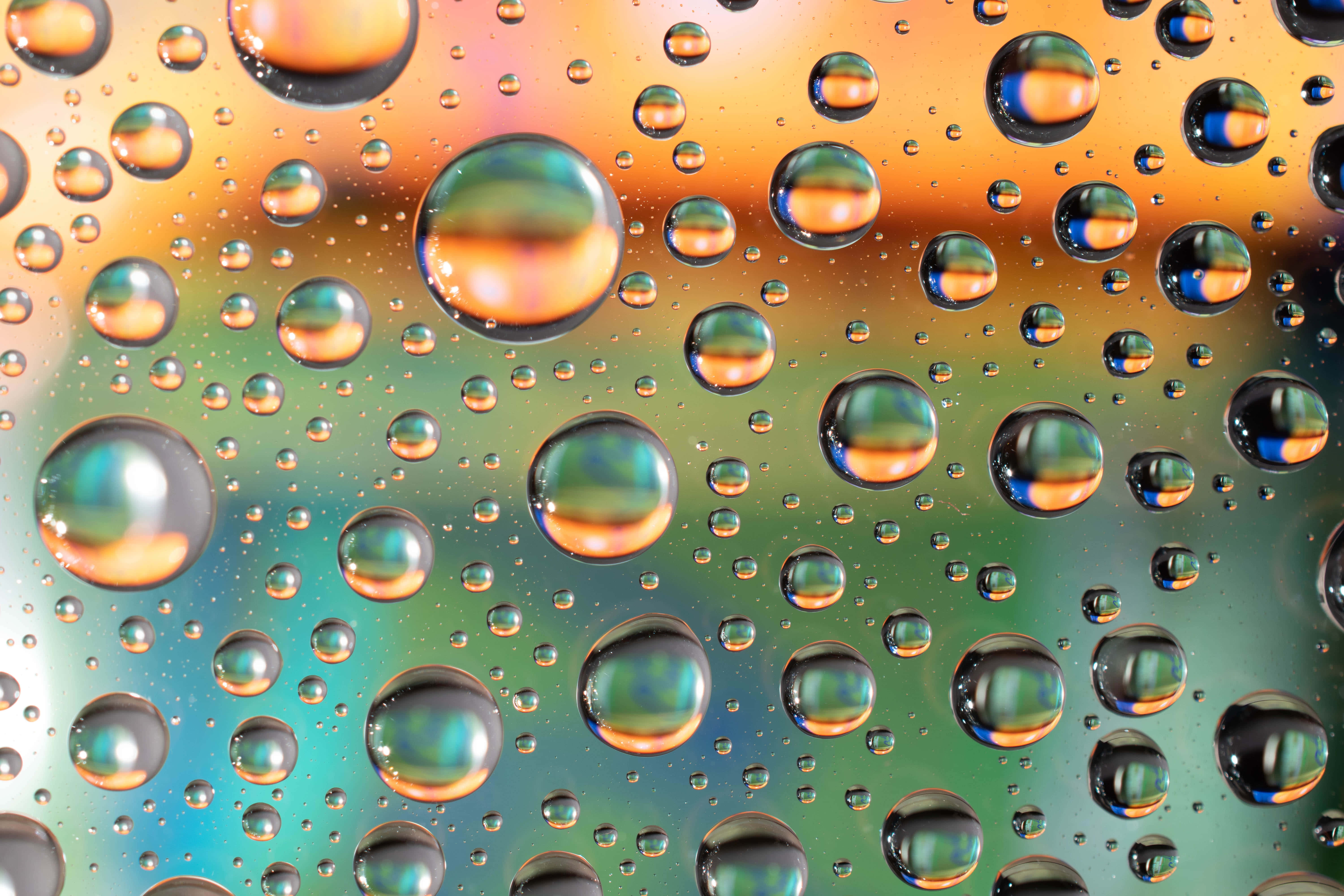 Liquid 桌布 壁紙 — 閃爍的水滴在光滑表面上折射出鮮豔的橙色、藍綠色和金色色調。