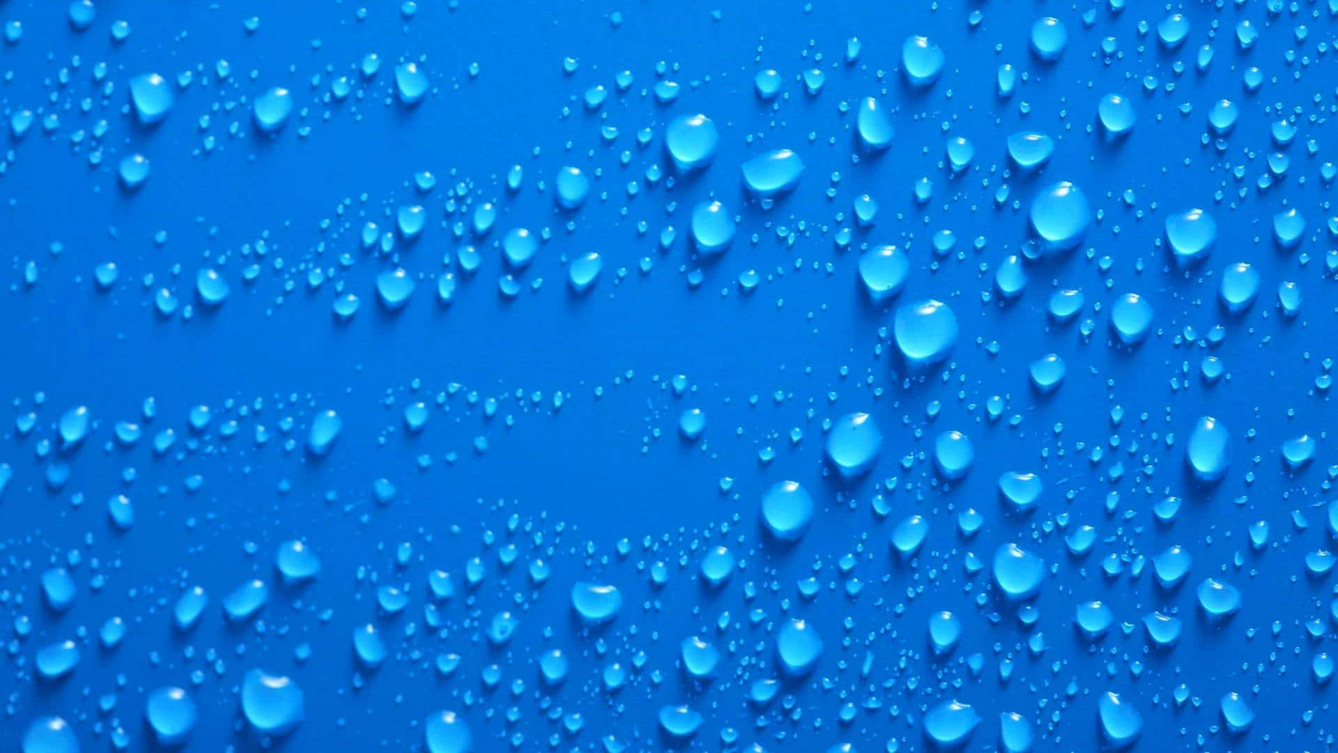 Plain Blue 桌布 壁紙 — 閃爍的水滴在鮮豔的藍色表面上散開，以球狀清晰度捕捉光線。