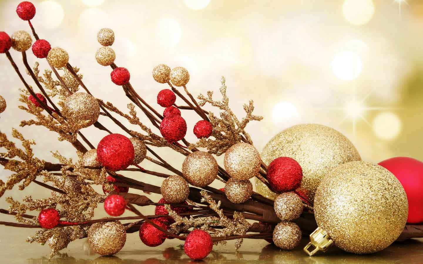 聖誕球 桌布 壁紙 — 閃爍的紅色和金色閃粉裝飾品和漿果排列在反光表面上，背景有溫暖的散景燈光。