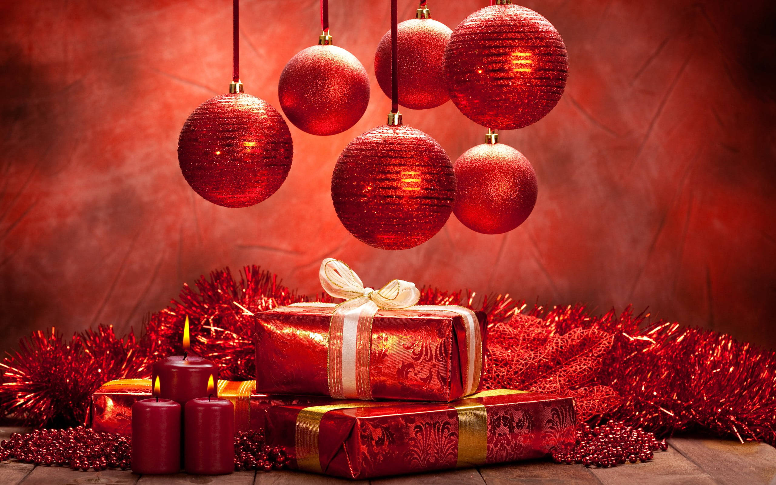 balls 桌布 壁紙 — 閃爍的紅色裝飾品懸掛在堆疊的禮品盒和點燃的蠟燭上方，背景是帶紋理的深紅色。