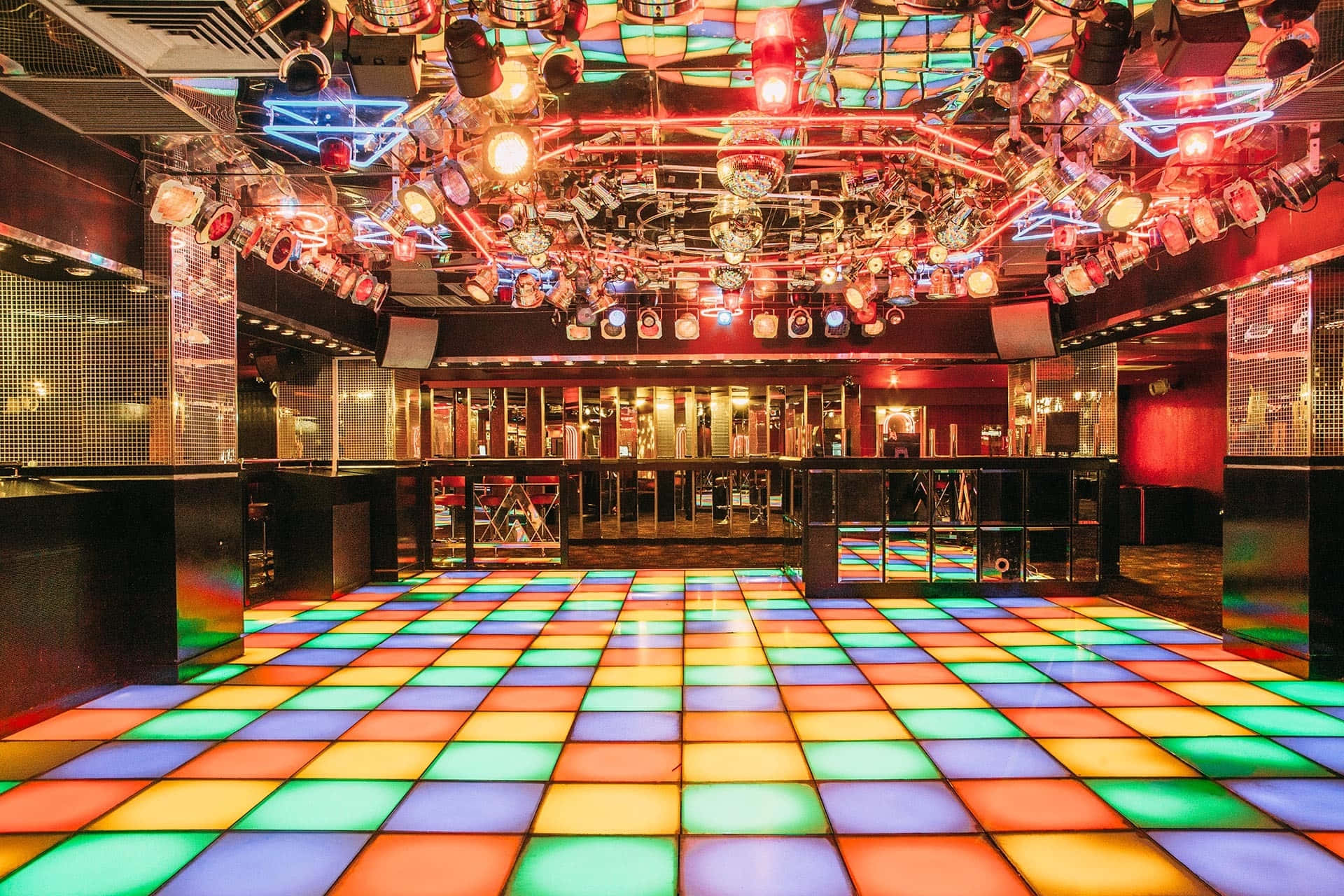 club 桌布 壁紙 — 閃爍的迪斯科球天花板和彩虹燈光舞池，搭配鏡面牆壁和舞台燈光，營造出充滿活力的夜總會場景。