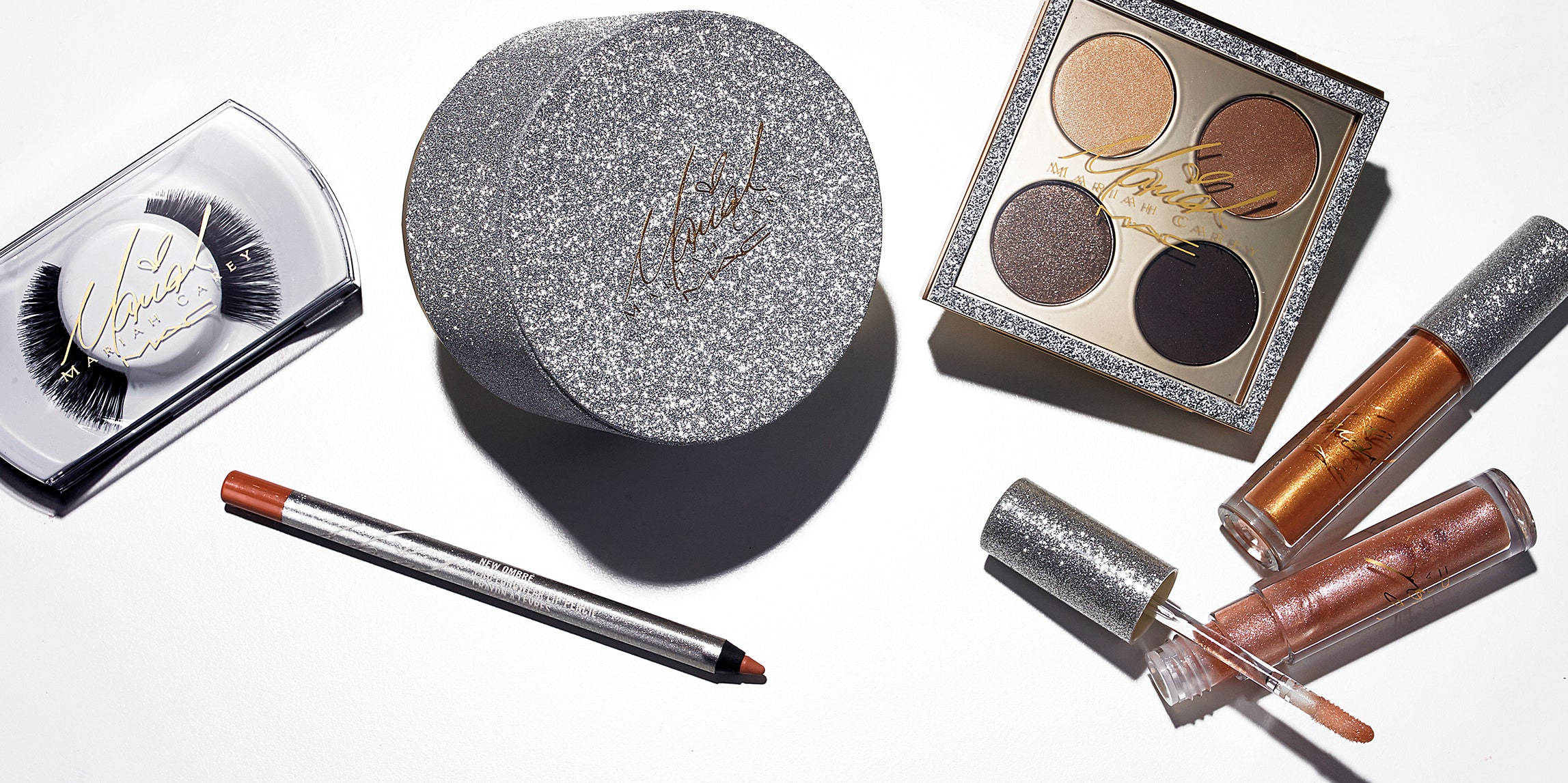 Cosmetics 桌布 壁紙 — 閃爍的銀色和古銅色化妝品，包括假睫毛、眼影盤、唇彩和眼線筆，排列在明亮的白色表面上。