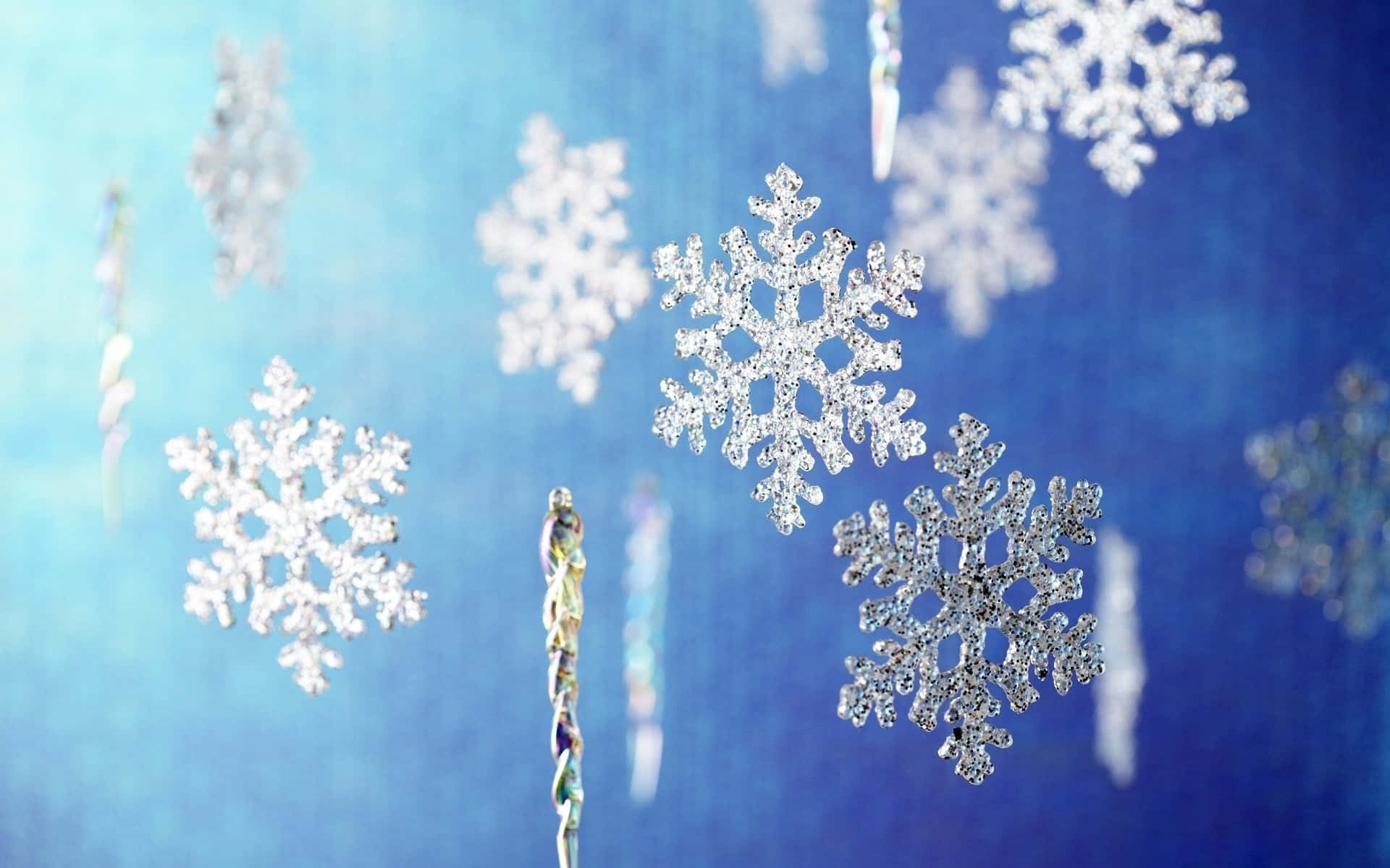 雪花 桌布 壁紙 — 閃爍的銀色雪花裝飾品懸掛在柔和的藍色漸變背景上，帶有微妙的散景效果。