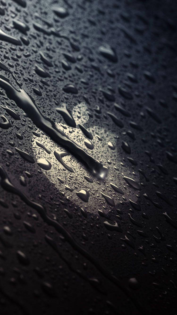 iPhone Se 桌布 壁紙 — 閃爍的雨滴在聚焦光束照射的黑暗表面上傾瀉而下，營造出陰鬱的反射場景。