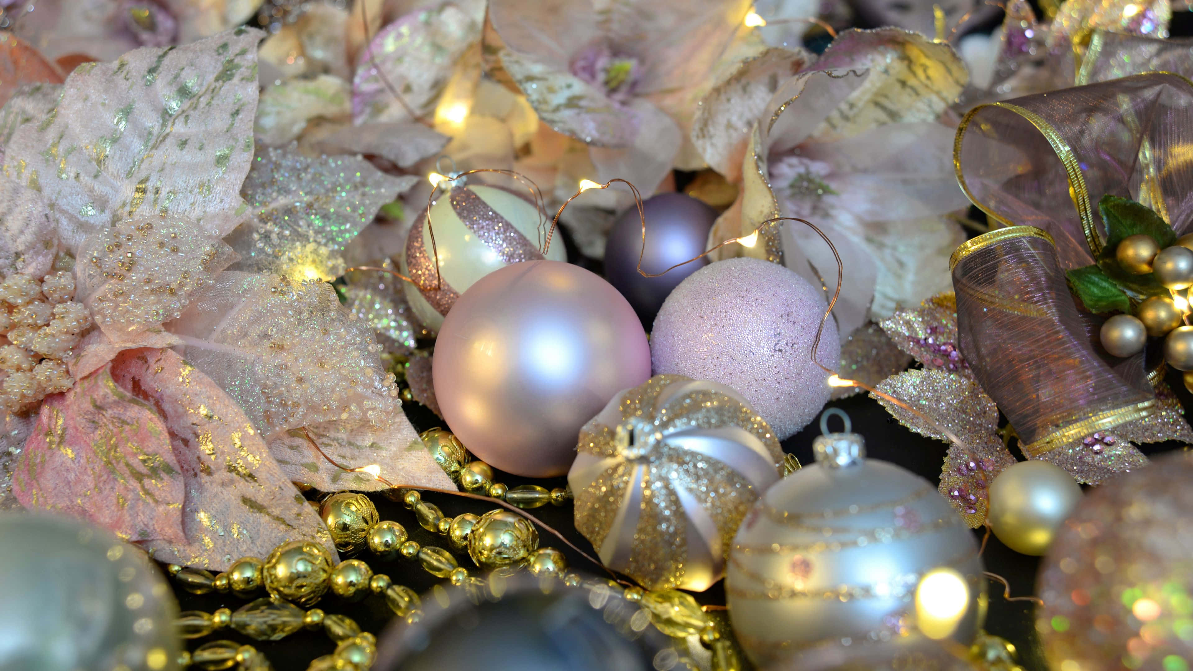 Rose Gold Christmas 桌布 壁紙 — 閃爍粉紅和銀色裝飾品的特寫，依偎在閃閃發光的粉紅花朵和金色珠子之間，伴隨著溫暖的仙女燈。