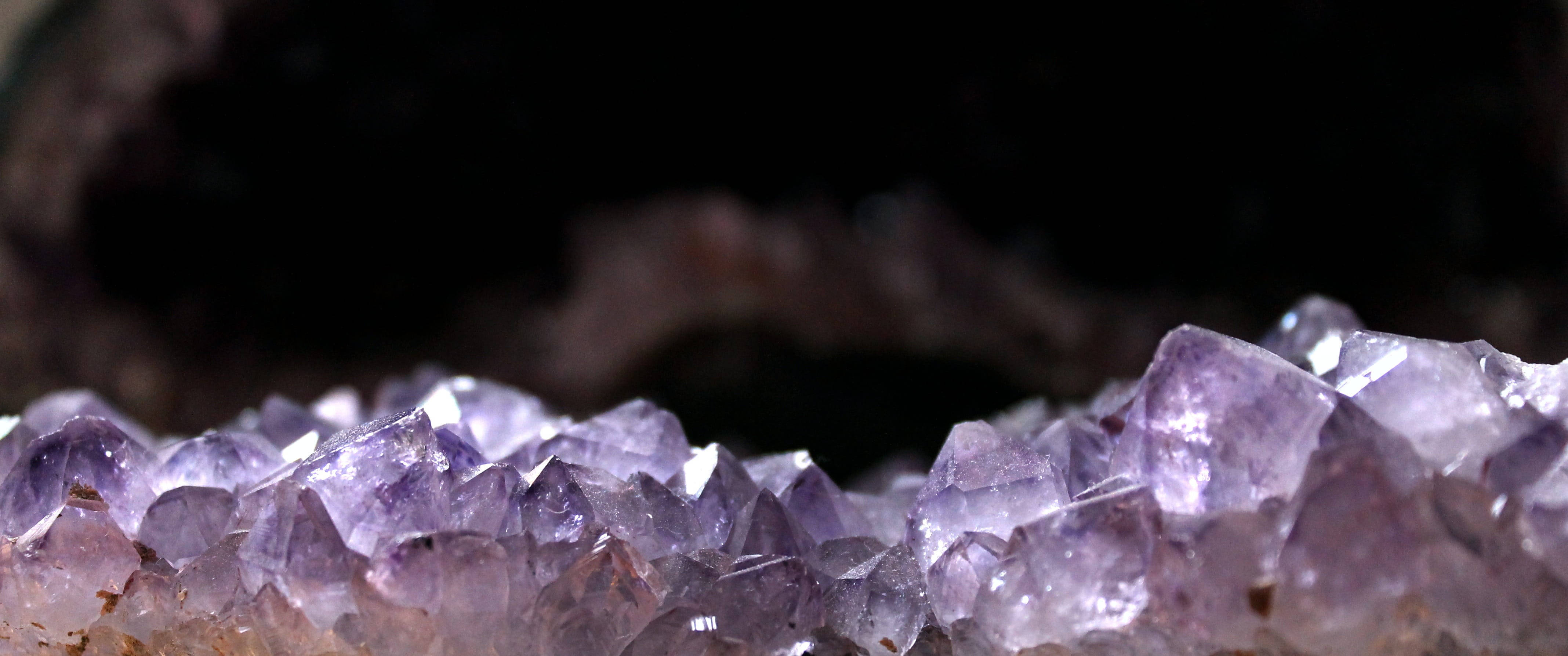 紫水晶 桌布 壁紙 — 閃爍紫色紫水晶晶體在黑暗洞穴背景中發光的特寫。