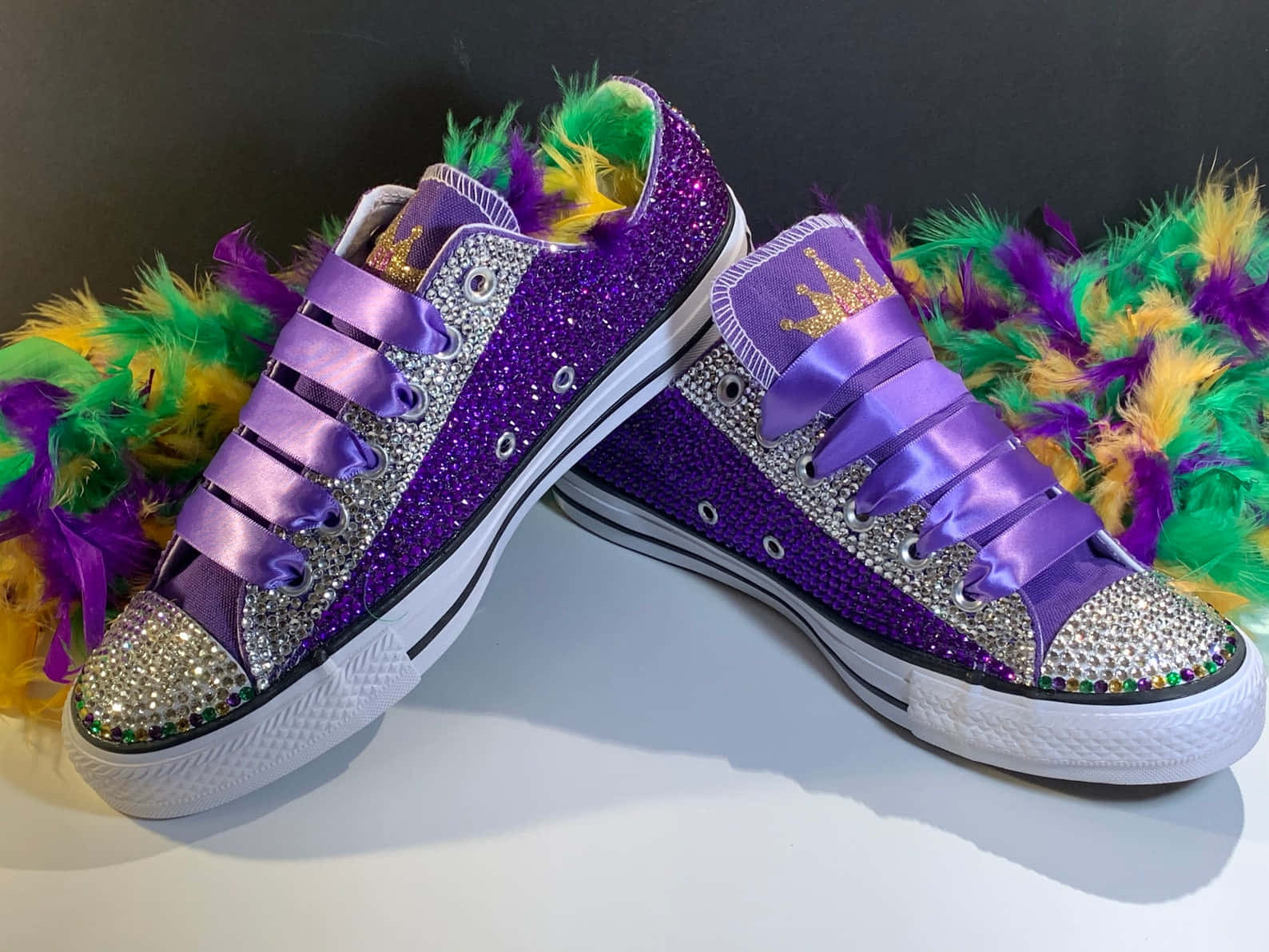 Purple Shoes 桌布 壁紙 — 閃爍紫色運動鞋飾有水鑽和緞面鞋帶，旁邊放有充滿活力的狂歡節羽毛。