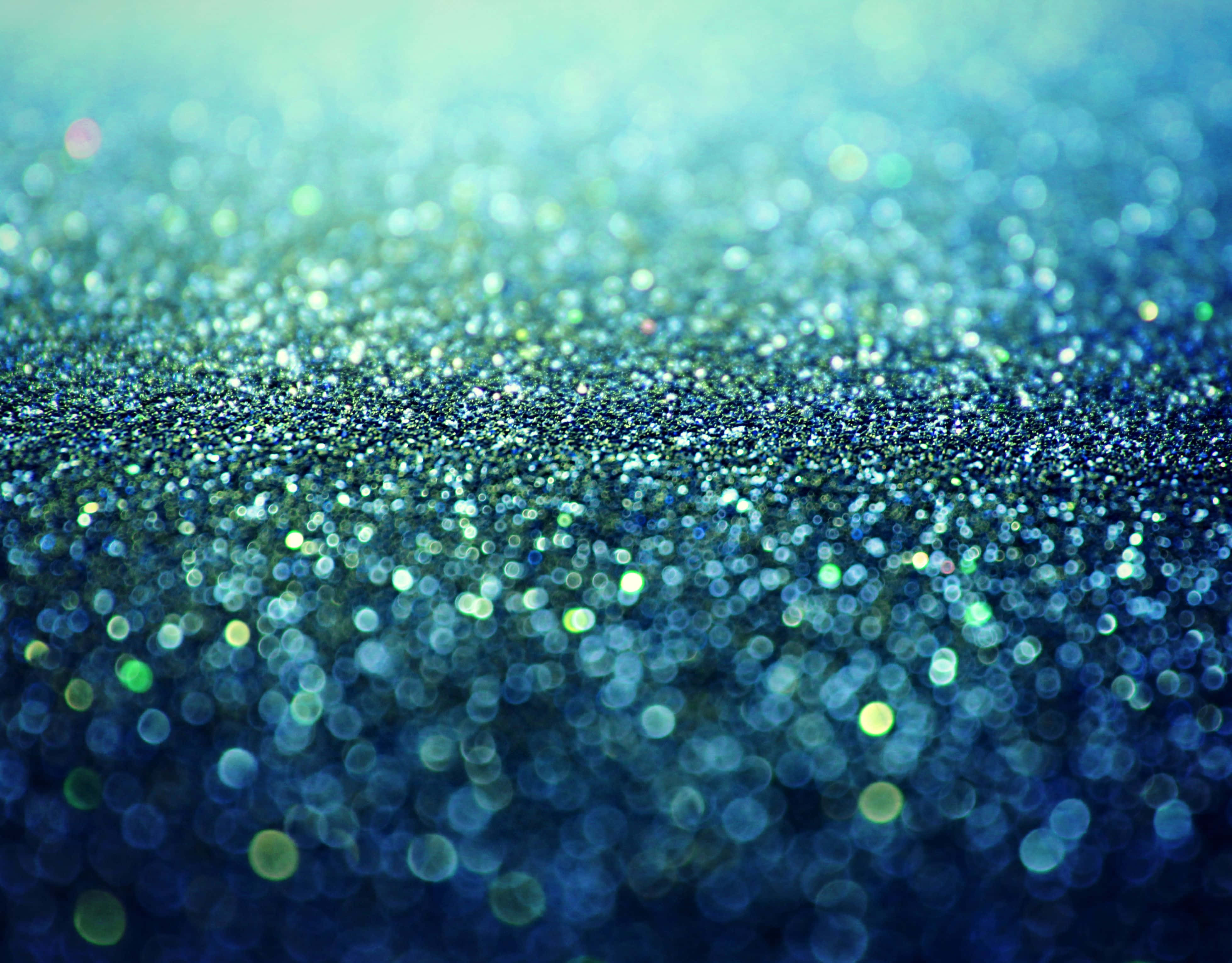 Teal Glitter 桌布 壁紙 — 閃爍藍色和綠色亮粉的特寫，帶有散景高光，營造出閃閃發光的紋理表面。