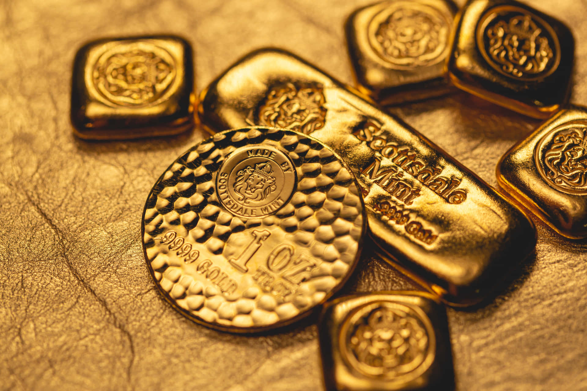 Shiny Gold 桌布 壁紙 — 閃爍金幣和金條的特寫，帶有精細雕刻，放置在紋理金色表面上。
