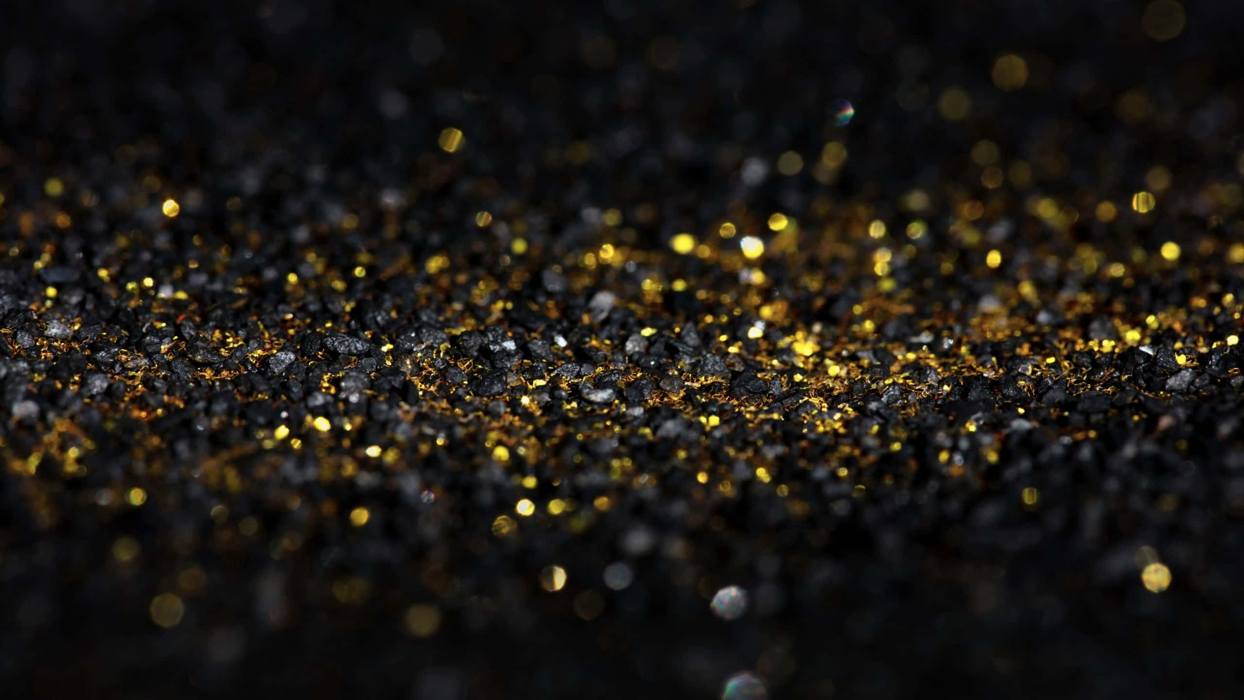 Black And Gold Glitter 桌布 壁紙 — 閃爍金色亮粉顆粒的特寫，散落在深黑色紋理表面上，帶有柔和散景。
