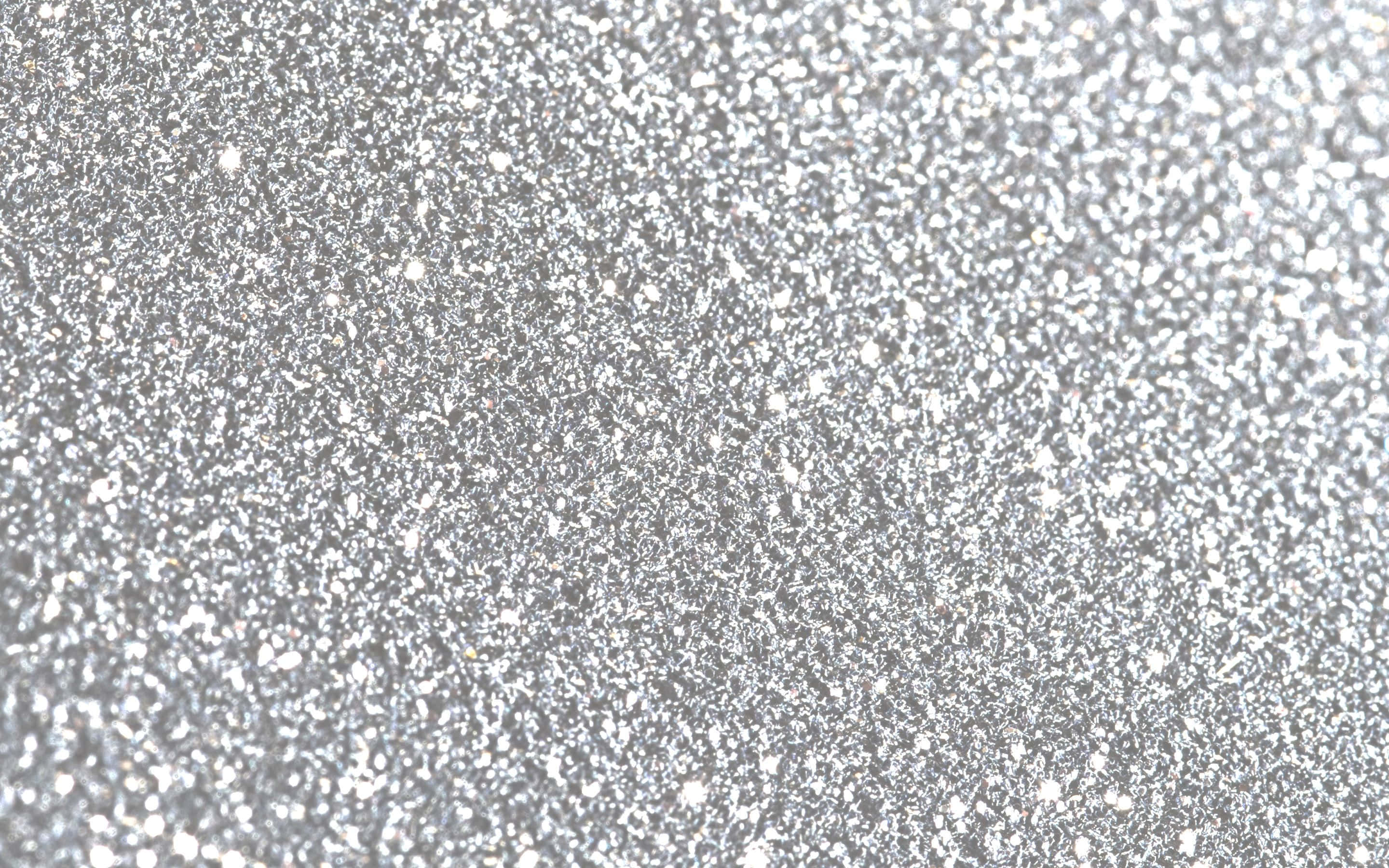 White Glitter 桌布 壁紙 — 閃爍銀色亮粉顆粒在紋理表面上捕捉光線的特寫。