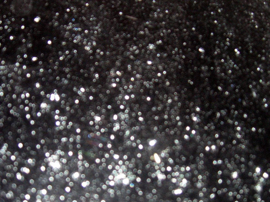 Glitter Black 桌布 壁紙 — 閃爍銀色亮粉顆粒散落在深色表面上的特寫，營造出閃閃發光的紋理效果。