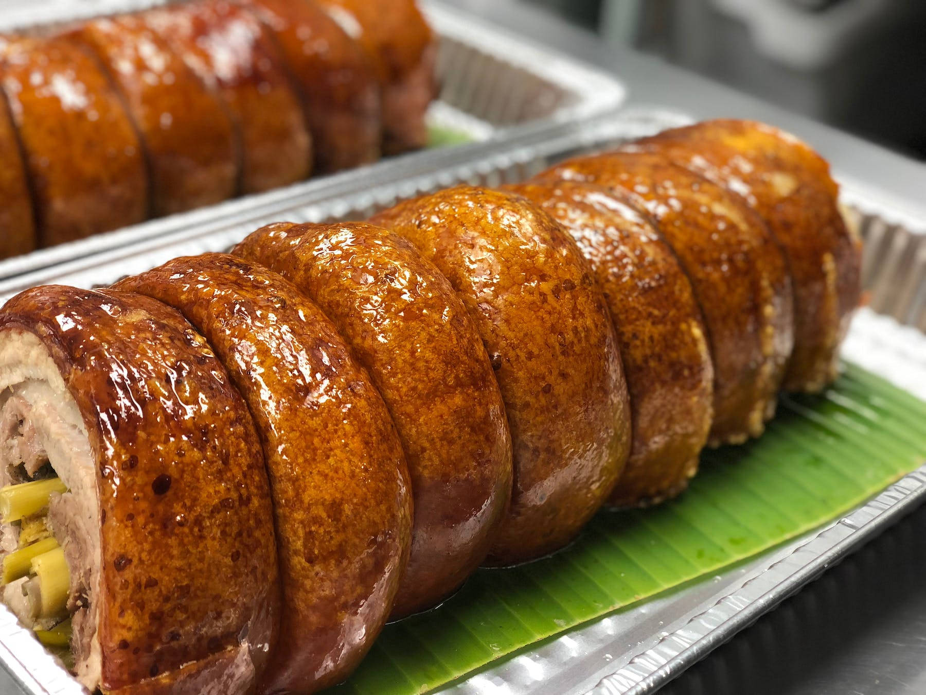 Pig 桌布 壁紙 — 閃閃發光的烤豬腩切成厚片，放在綠色香蕉葉上，置於金屬托盤中。