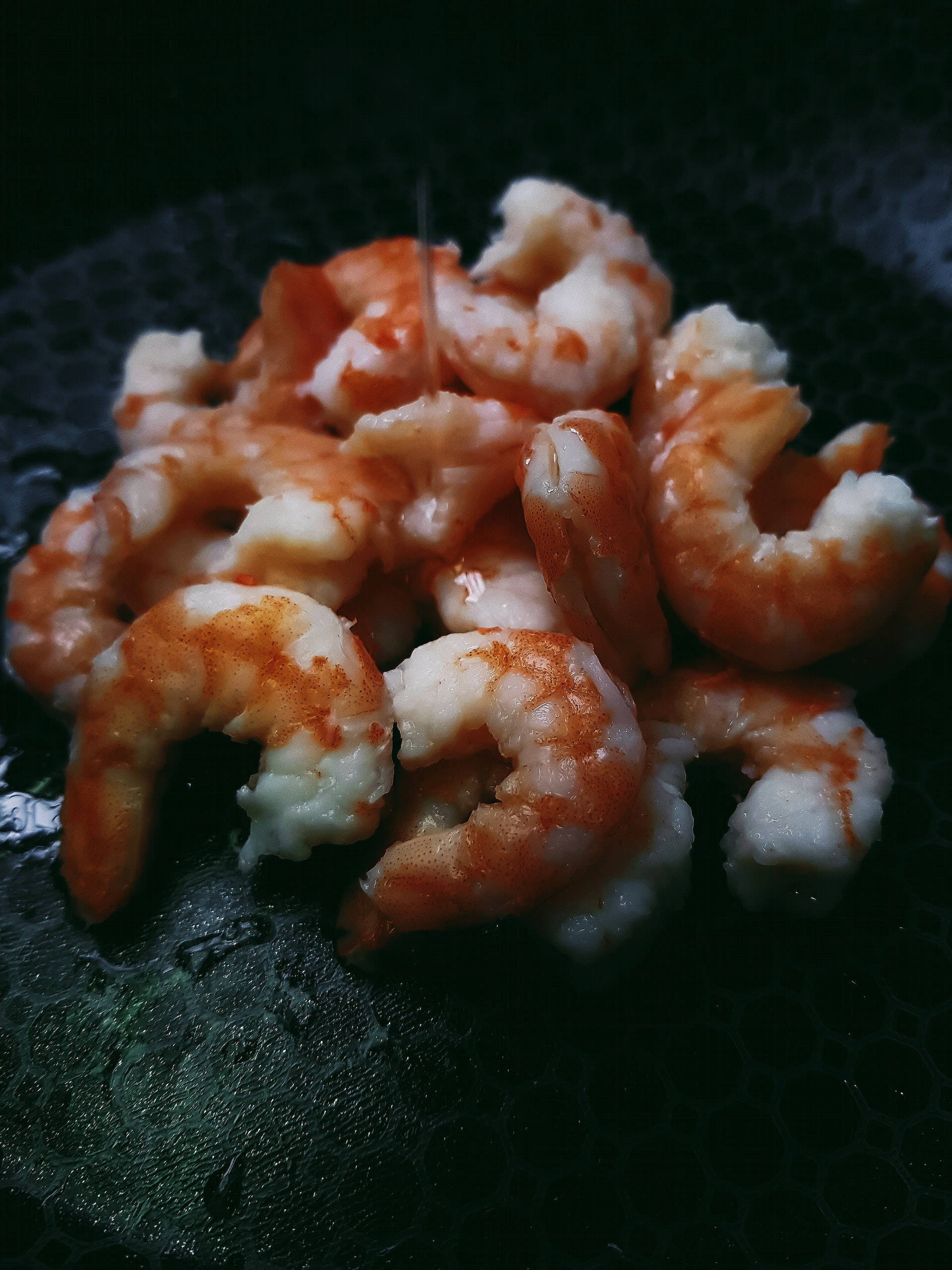 yummy 桌布 壁紙 — 閃閃發光的熟蝦，橙色尾巴，堆疊在深色紋理盤子上，在戲劇性燈光下。
