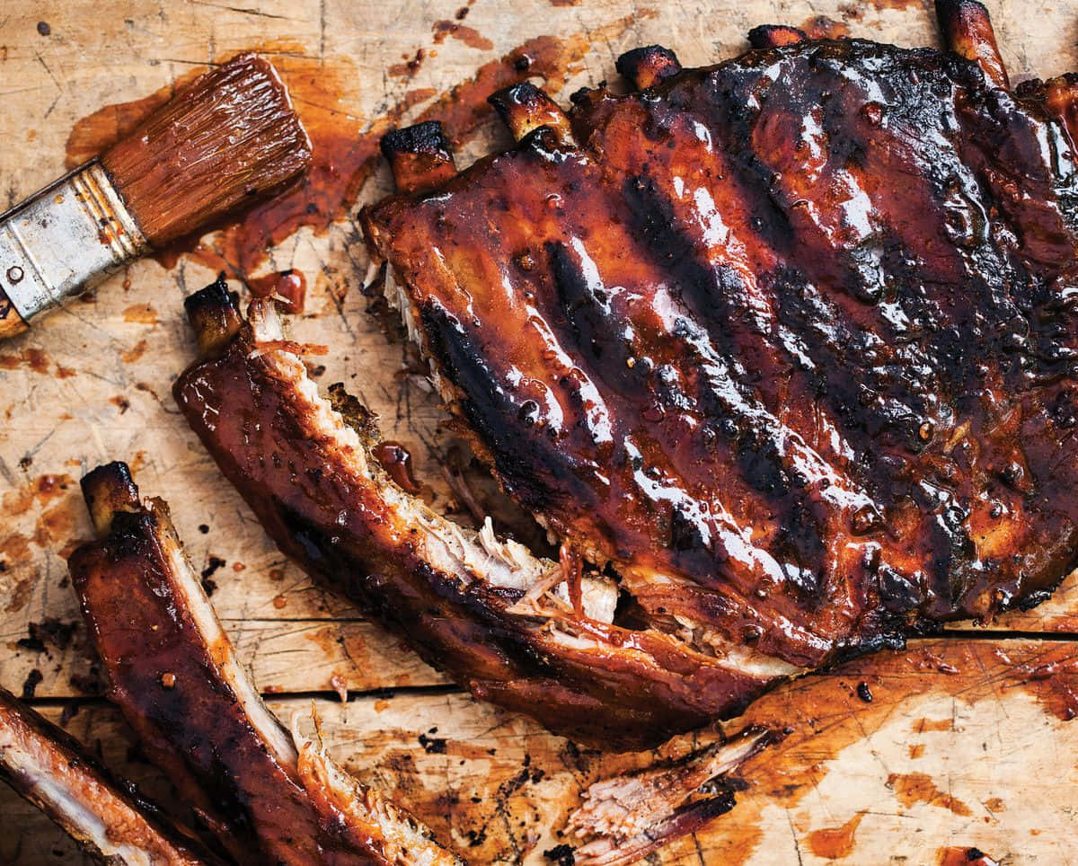 Bbq 桌布 壁紙 — 閃閃發光的燒烤肋骨帶有焦糖釉面，放在一塊風化的木板上，旁邊有一把用過的塗抹刷。