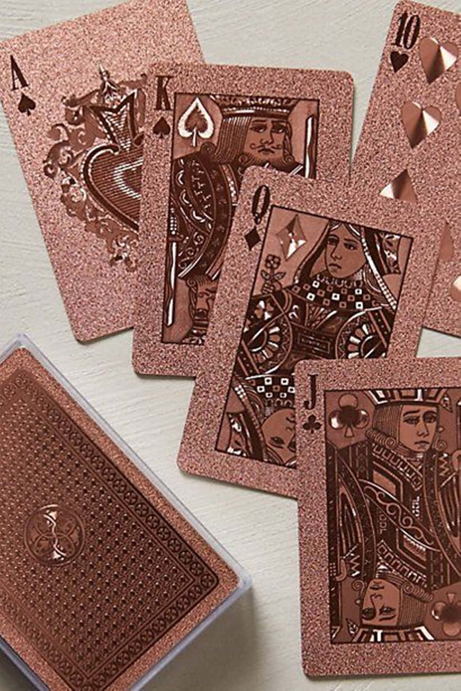 Rose Gold Color 桌布 壁紙 — 閃閃發光的玫瑰金色撲克牌在淺色木面上扇狀展開，顯示國王、皇后和傑克，帶有華麗設計。