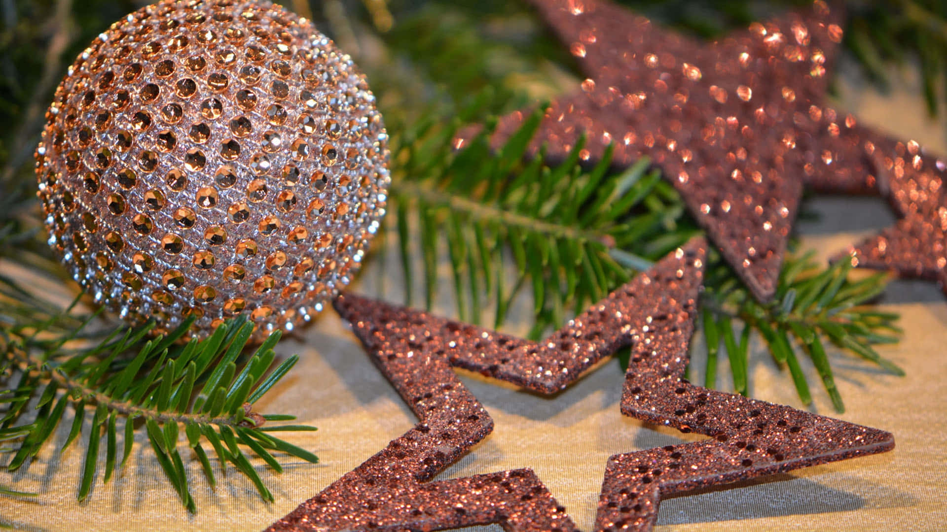 Christmas Star 桌布 壁紙 — 閃閃發光的玫瑰金飾品和星星裝飾品放在松針上，背景是帶紋理的米色表面。
