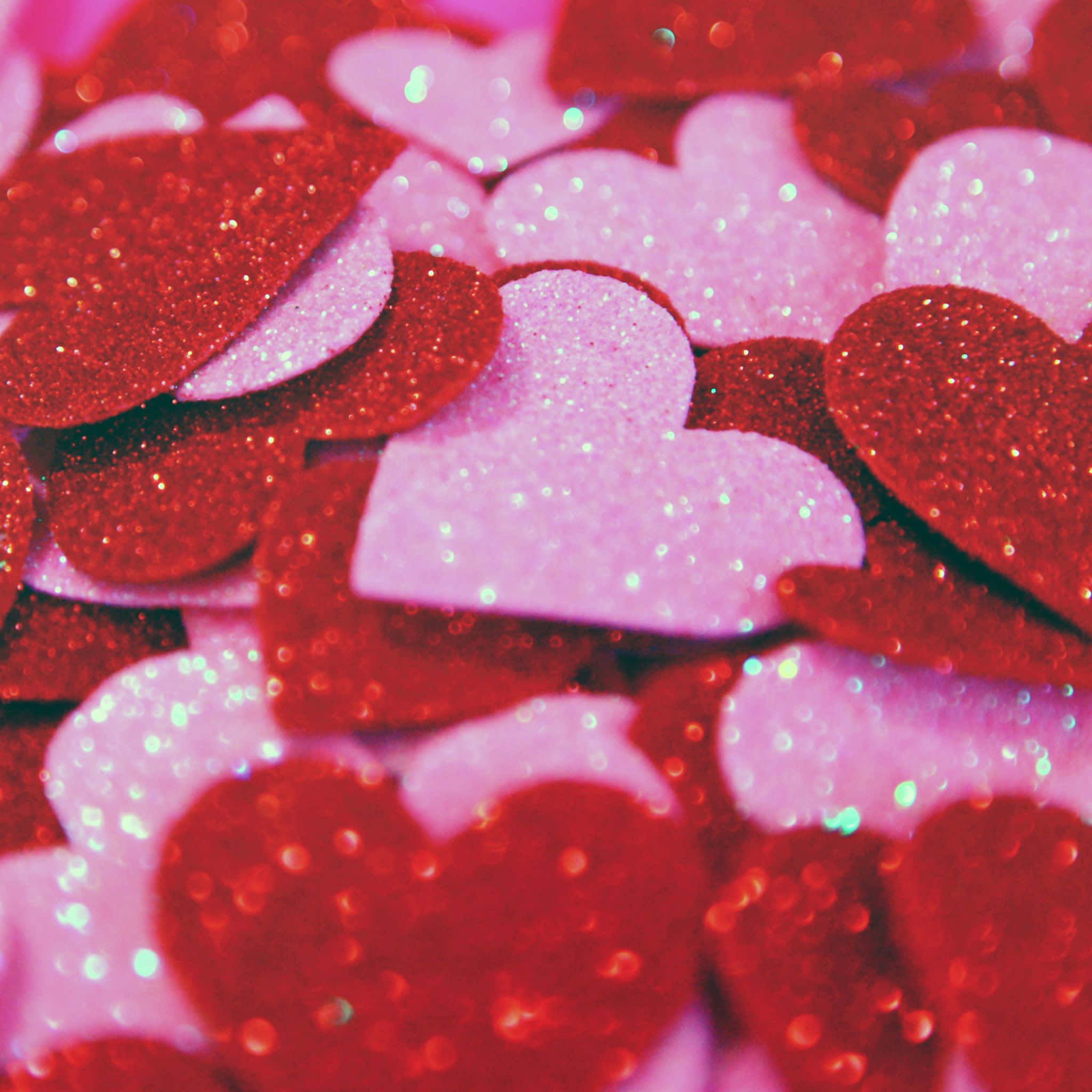 Red Hearts 桌布 壁紙 — 閃閃發光的紅色和粉紅色心形紙屑在柔和光線下閃爍的特寫。
