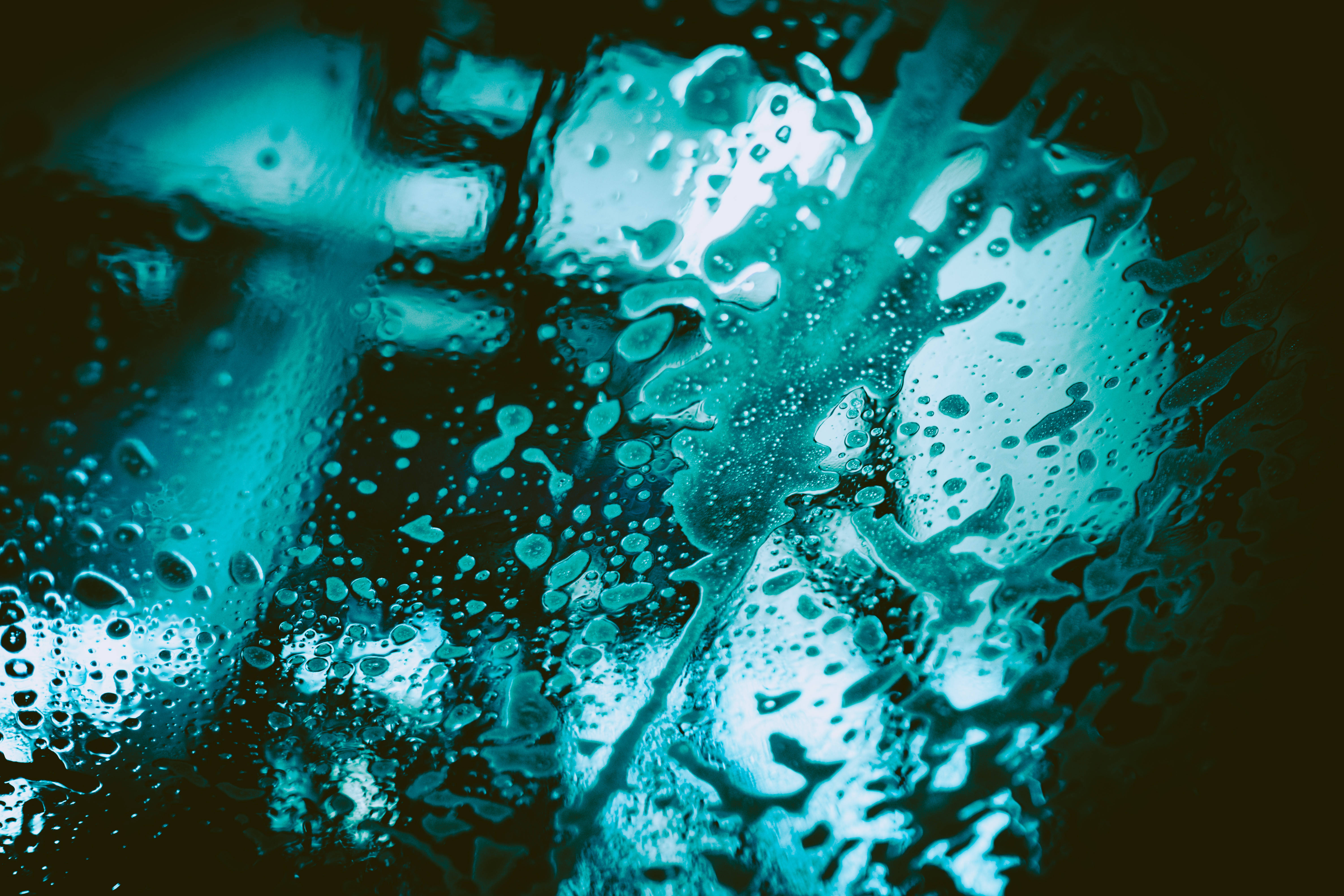 Droplets 桌布 壁紙 — 閃閃發光的藍綠色水滴在深色背景的玻璃表面上傾瀉而下。