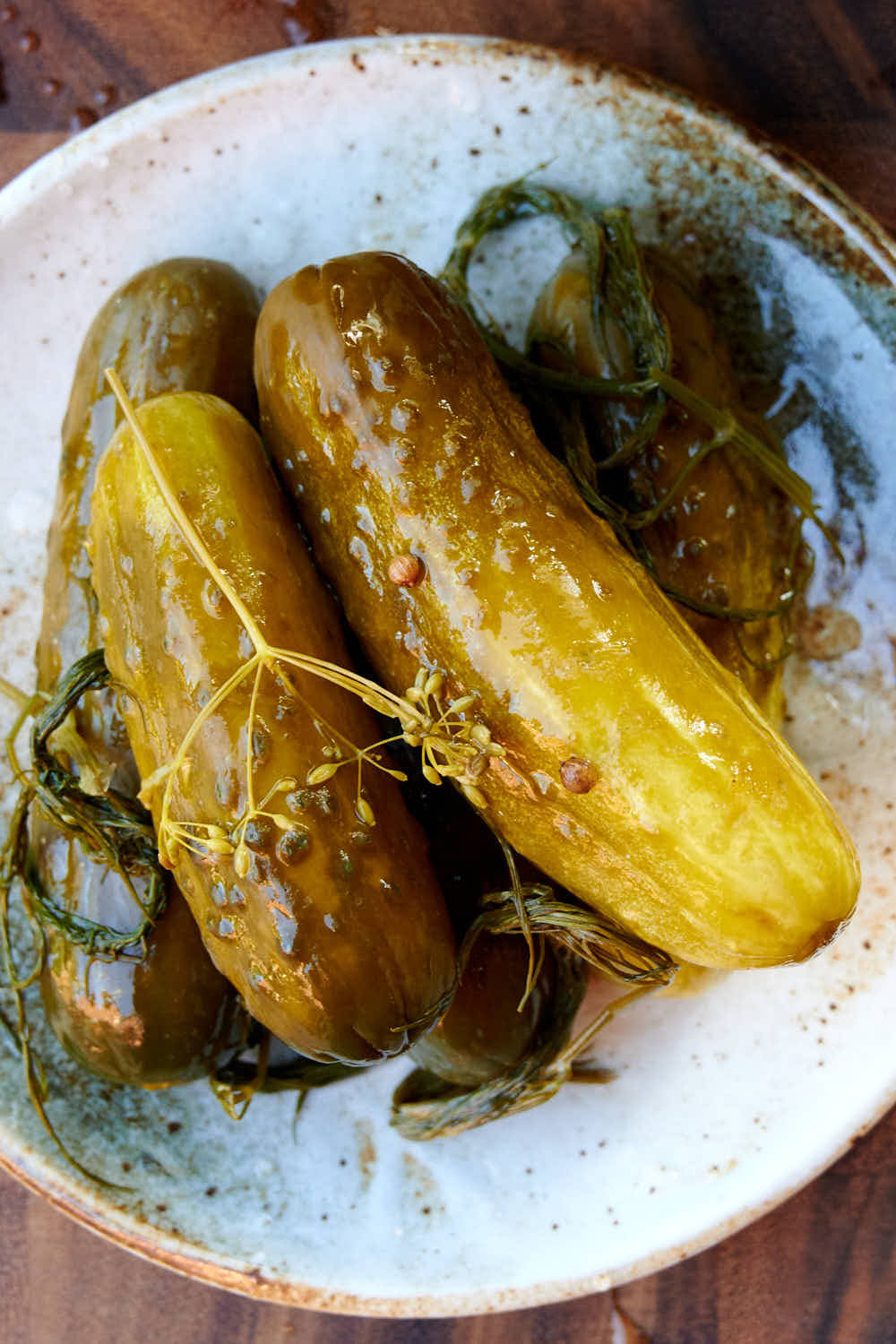 醃黃瓜 桌布 壁紙 — 閃閃發光的醃黃瓜配蒔蘿和胡椒粒，放在木質表面上的斑點陶瓷碗中。