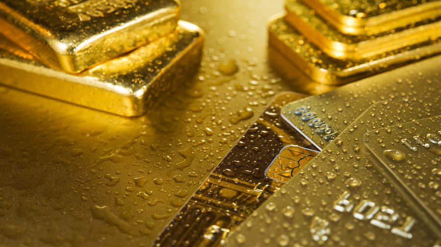 Shiny Gold 桌布 壁紙 — 閃閃發光的金條和信用卡在反光的金色表面上閃爍著水滴。