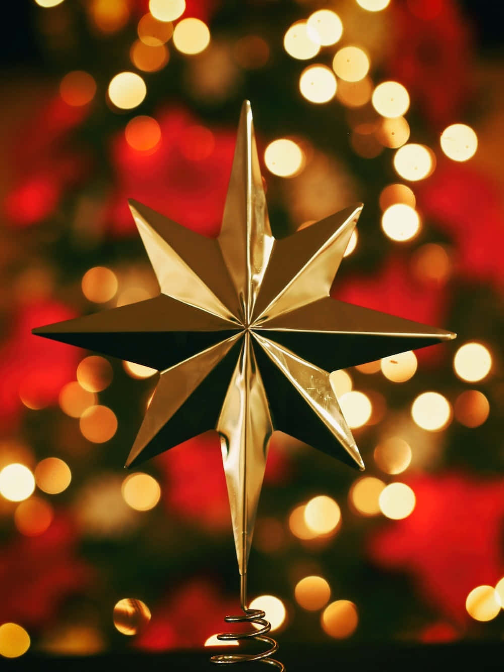 Gold Star 桌布 壁紙 — 閃閃發光的金色星星樹頂裝飾，在紅色和金色燈光的溫暖散景中顯得格外清晰。