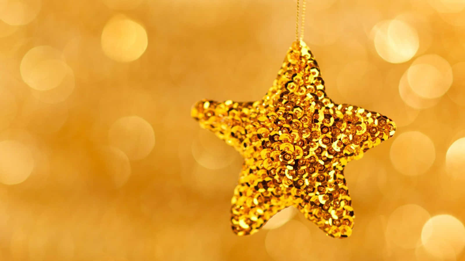 Gold Stars 桌布 壁紙 — 閃閃發光的金色星星裝飾掛在溫暖金色燈光的柔和散景背景上。