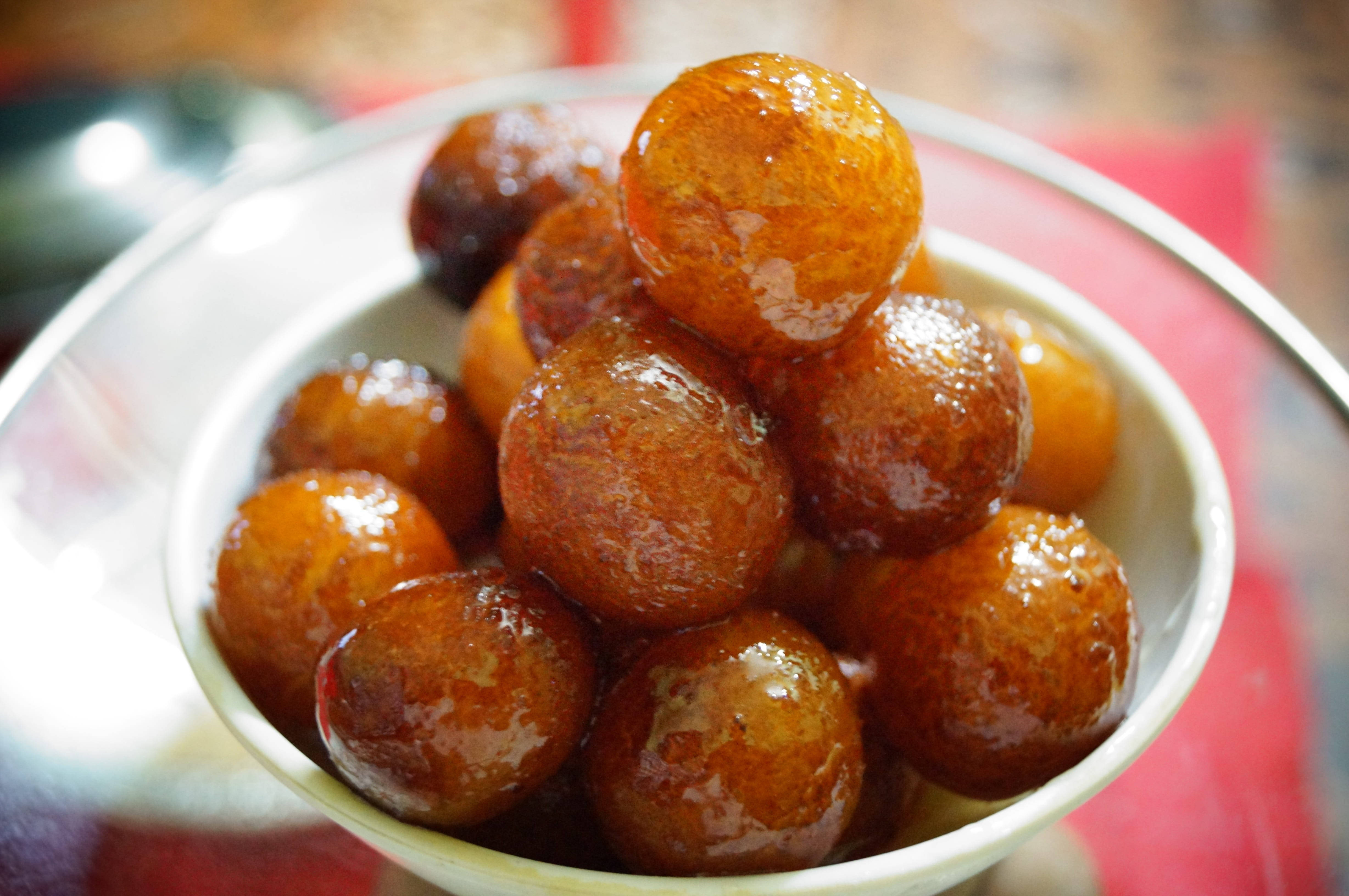 Indian 桌布 壁紙 — 閃閃發光的金色糖漿包裹的 gulab jamun 高高堆疊在紅色布上的白色碗中。