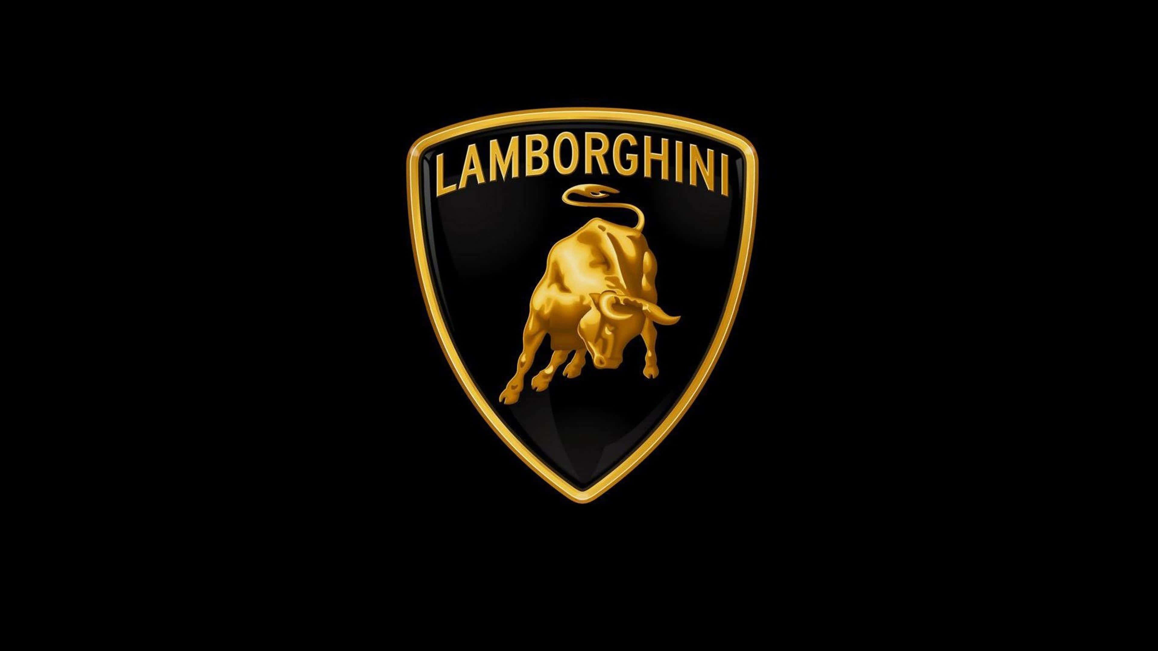 Car Logo 桌布 壁紙 — 閃閃發光的金色藍寶堅尼標誌，中央有一個衝鋒的公牛徽章，位於黑色背景上。