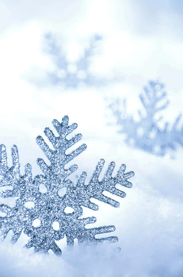 雪 桌布 壁紙 — 閃閃發光的銀色雪花躺在柔軟的白雪上，背景有模糊的雪花。