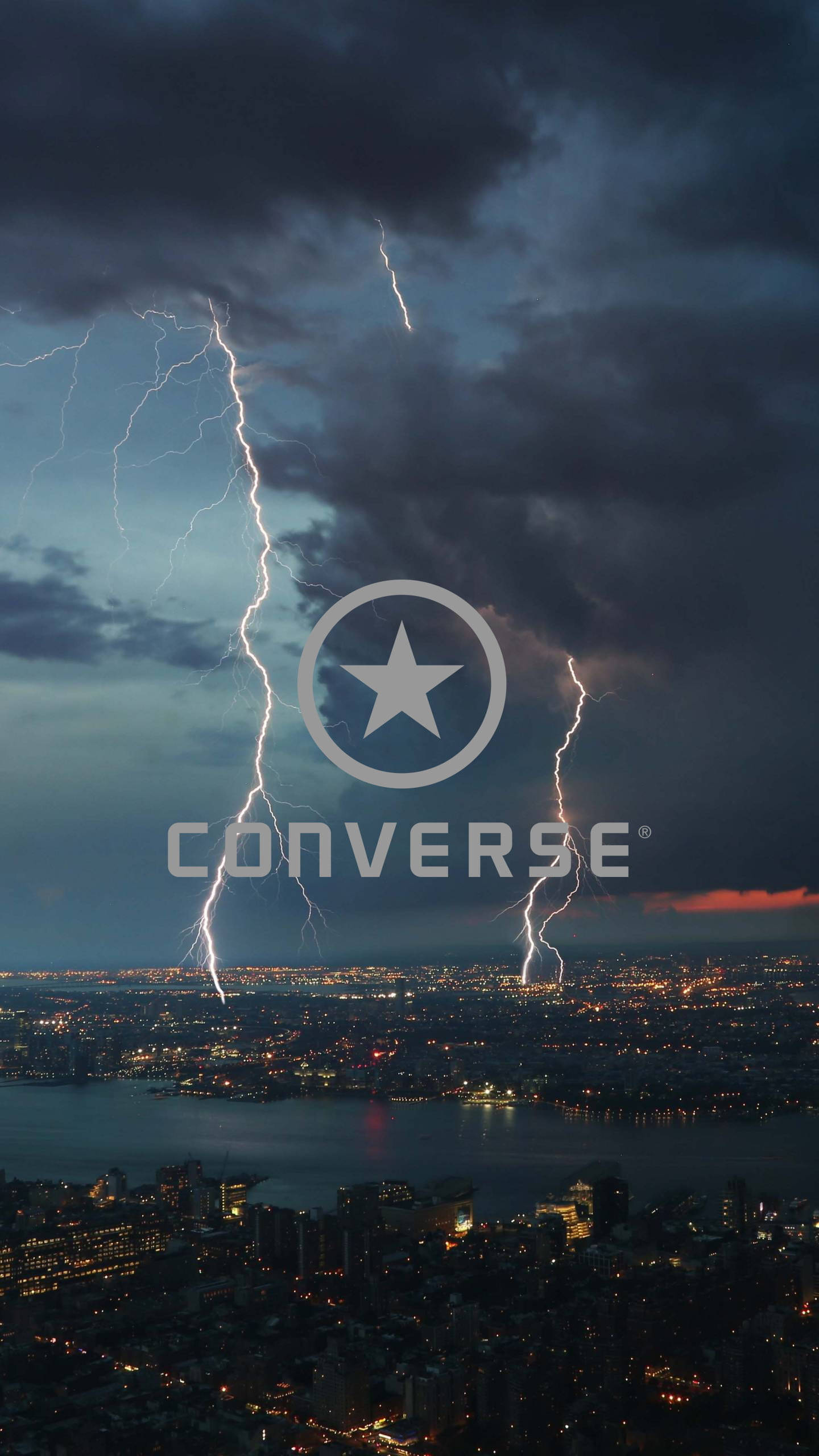 Converse 標誌 桌布 壁紙 — 閃電照亮暴風雨的天空，下方是夜晚中燈火輝煌的廣闊城市景觀。