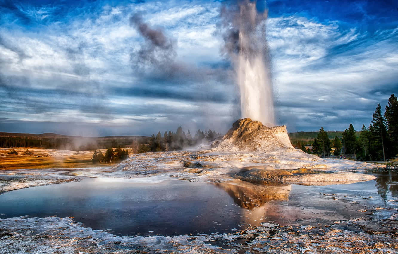 Yellowstone Geysers 桌布 壁紙 — 間歇泉在陰沉天空下戲劇性地噴發，蒸氣在礦物條紋景觀和反射水池上方升起。
