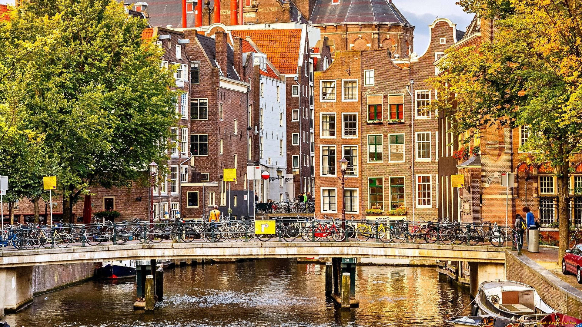Europe 桌布 壁紙 — 阿姆斯特丹充滿活力的運河景色，歷史悠久的磚砌建築，橋上排列的自行車，以及倒映在水中的秋樹。
