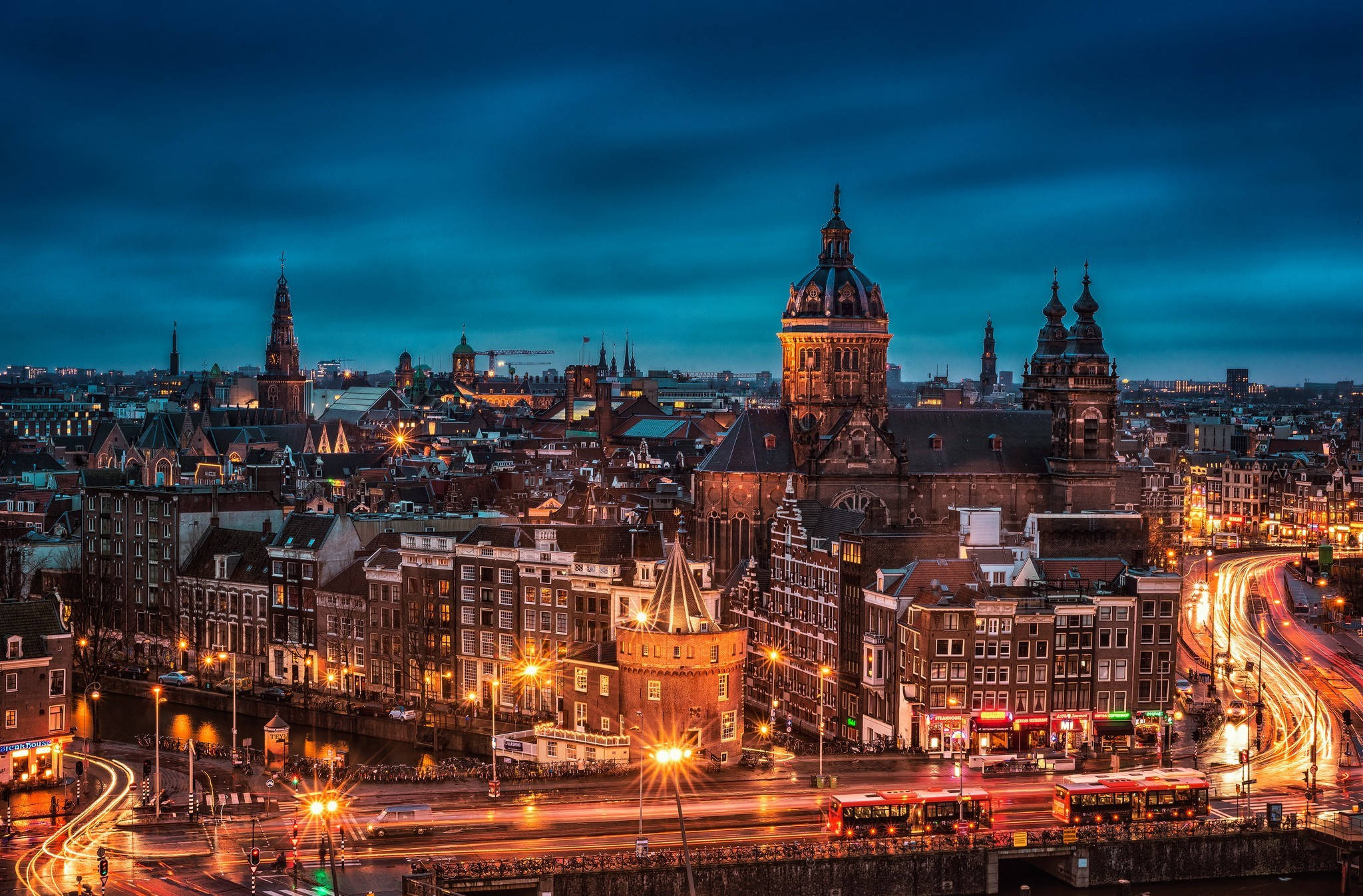 Netherlands 桌布 壁紙 — 阿姆斯特丹充滿活力的黃昏城市景觀，在深藍色天空下，閃爍的街燈和歷史建築交相輝映。