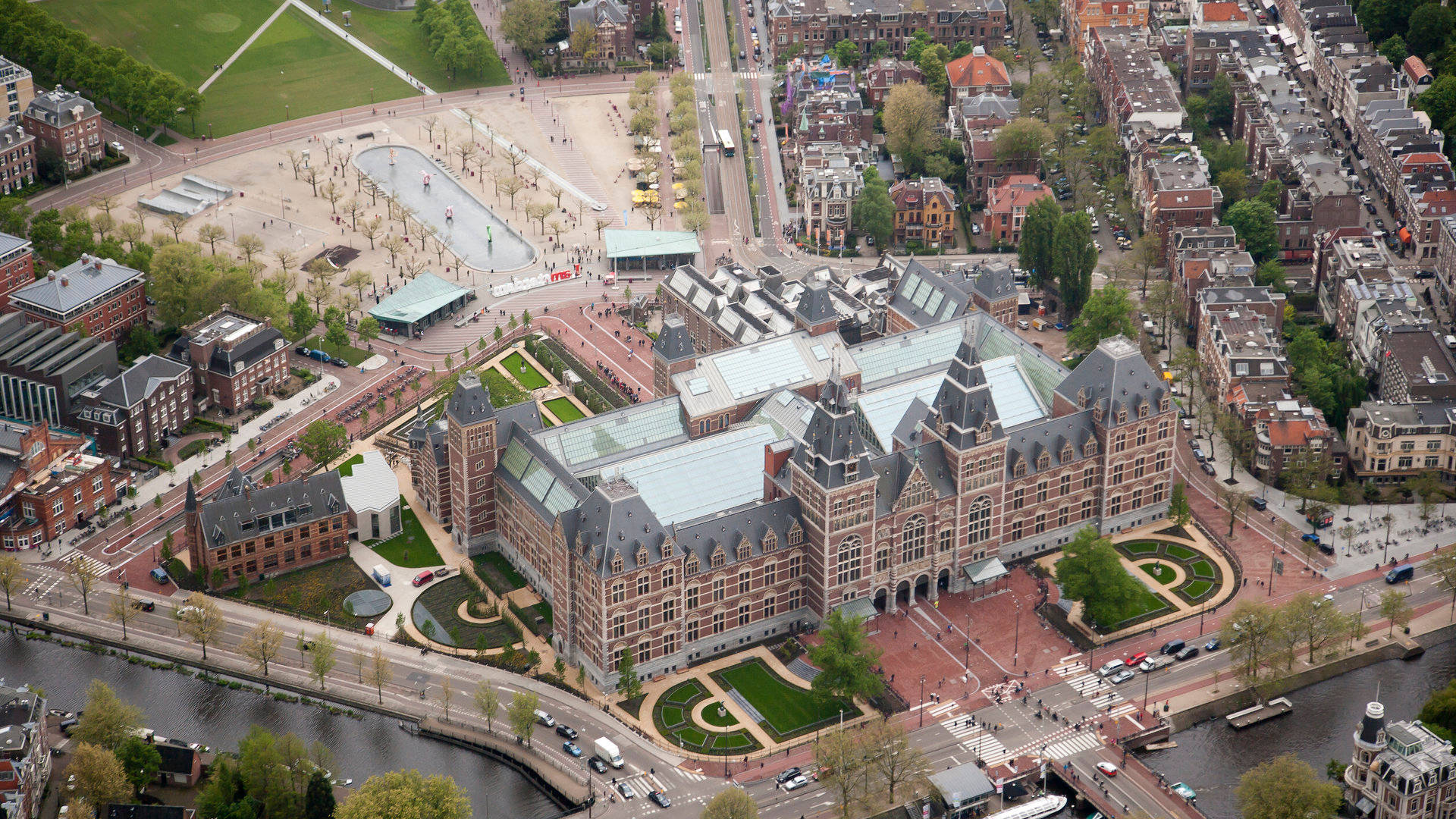Museum 桌布 壁紙 — 阿姆斯特丹國立博物館（Rijksmuseum）的鳥瞰圖，周圍環繞著運河、歷史建築、綠色花園和行人。