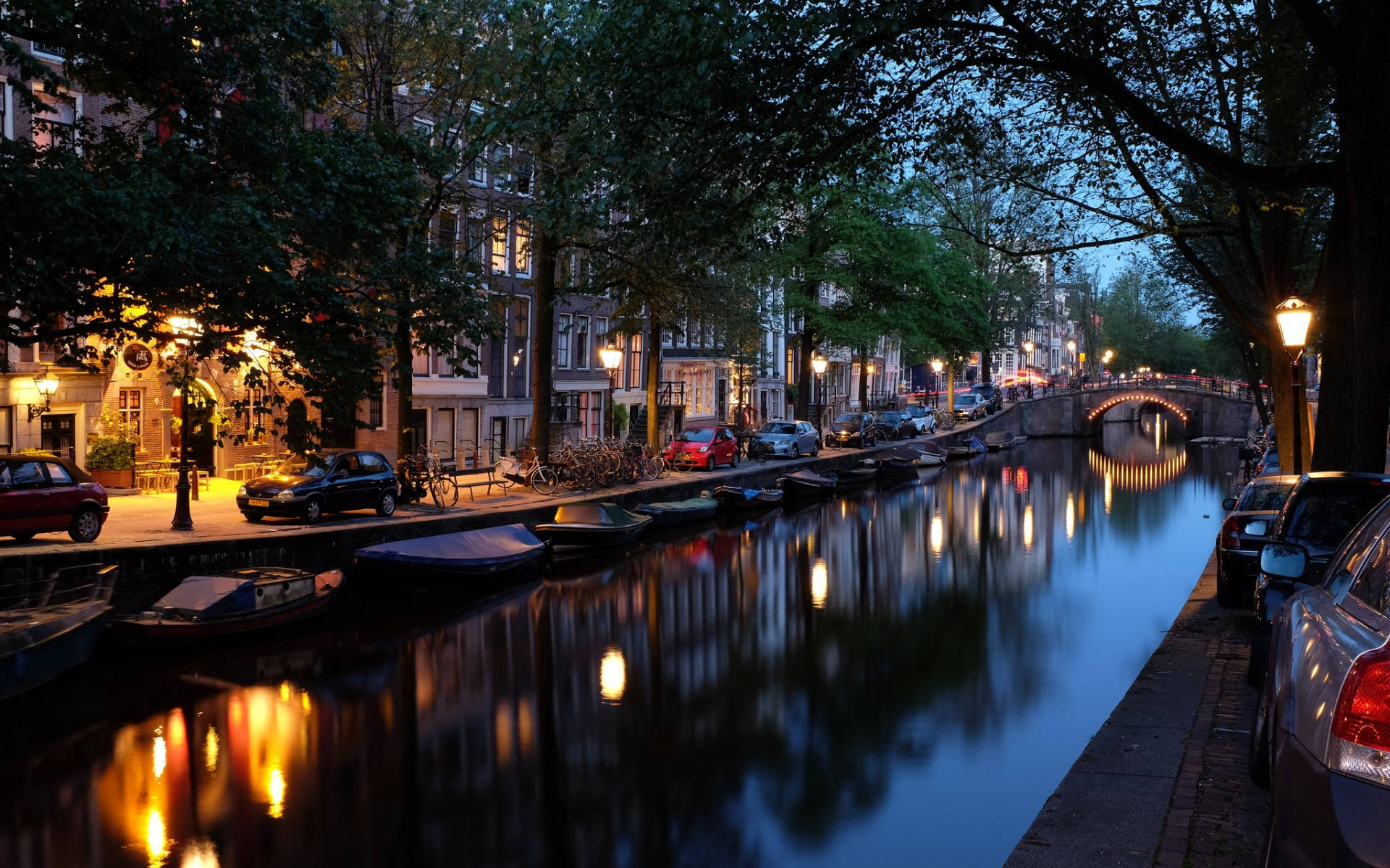 Netherlands 桌布 壁紙 — 阿姆斯特丹寧靜的黃昏運河，在深藍色天空下反射出溫暖的街燈和歷史建築。