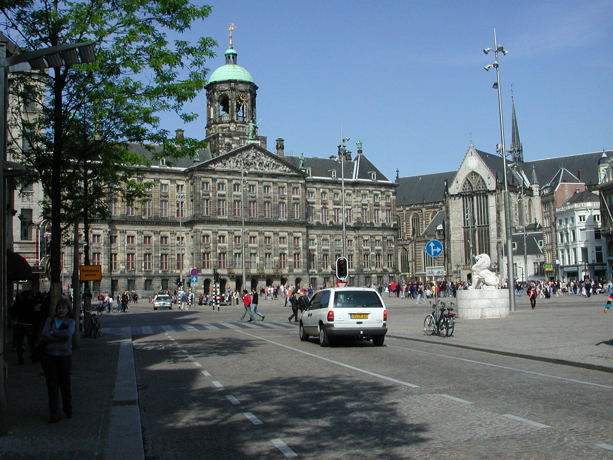 Amsterdam 桌布 壁紙 — 阿姆斯特丹水壩廣場的晴朗日子，歷史建築、熙攘的行人，以及鵝卵石街道上的白色貨車。