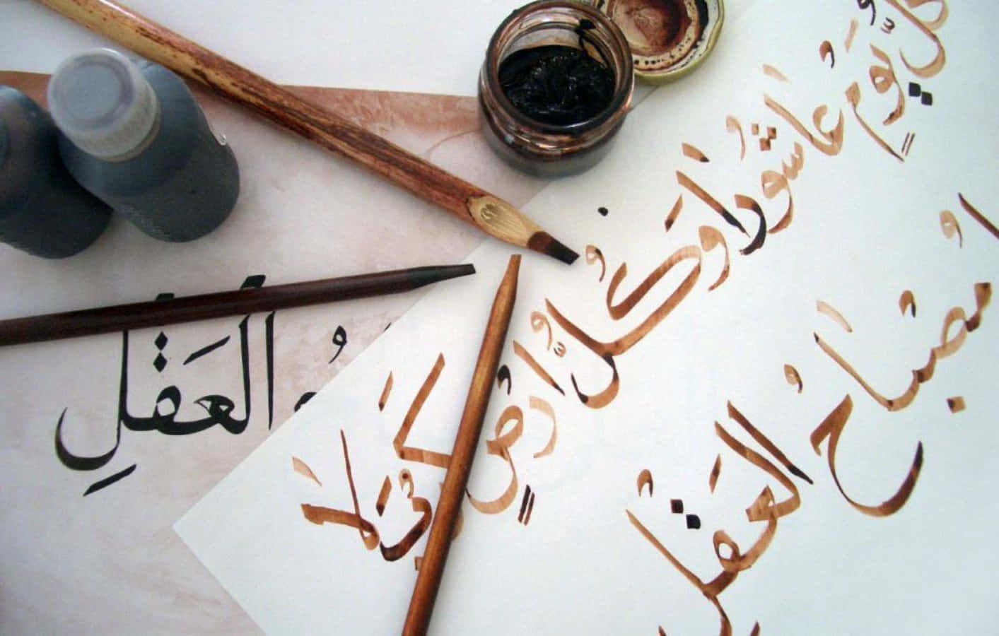 arabic 桌布 壁紙 — 阿拉伯書法工具和墨水在羊皮紙上的特寫，帶有黑色和棕色的流暢字體。