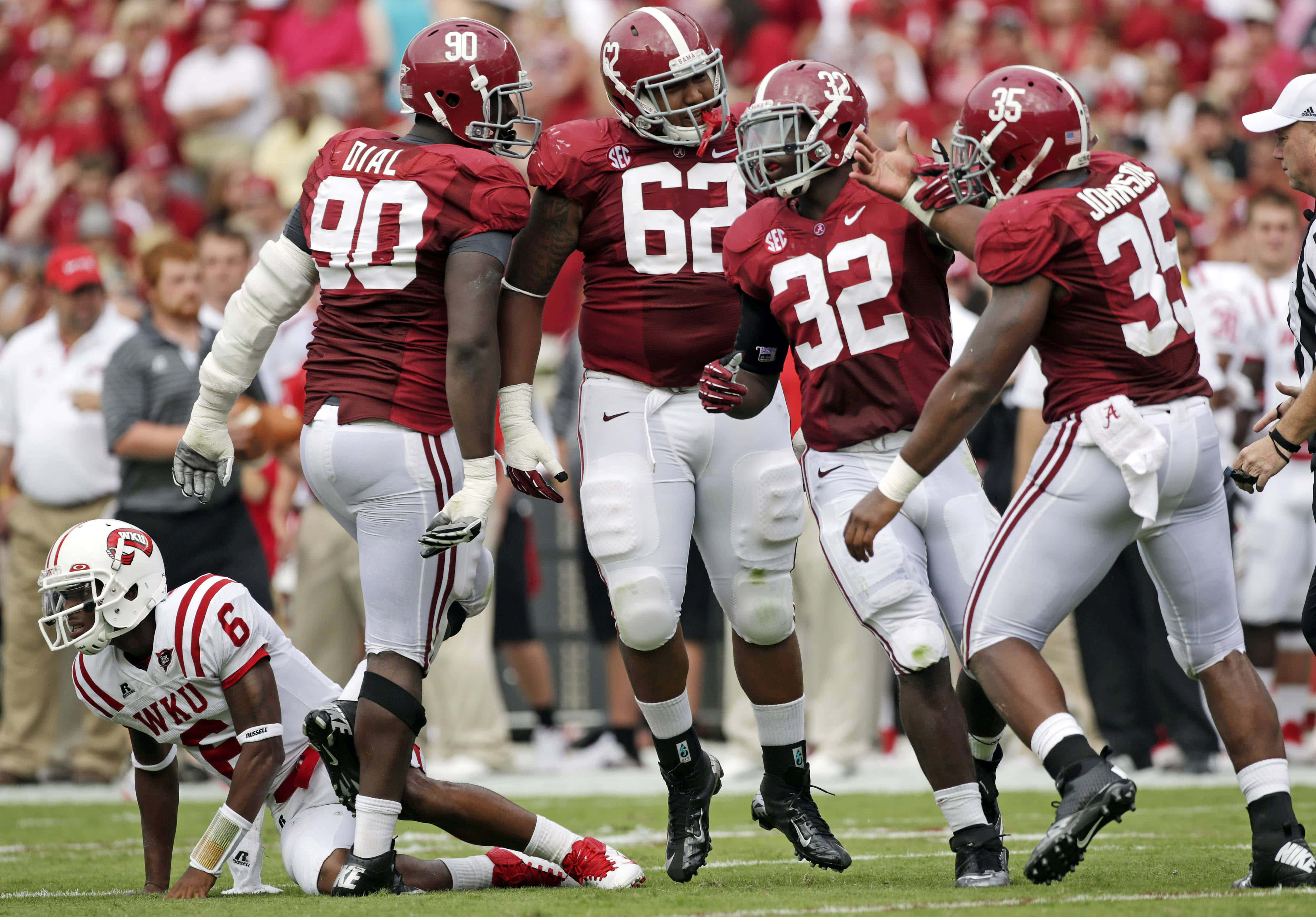 Alabama Football 桌布 壁紙 — 阿拉巴馬大學美式足球員身穿深紅色和白色裝備，在陽光明媚的球場上慶祝一次進攻，附近有一名倒下的WKU球員。