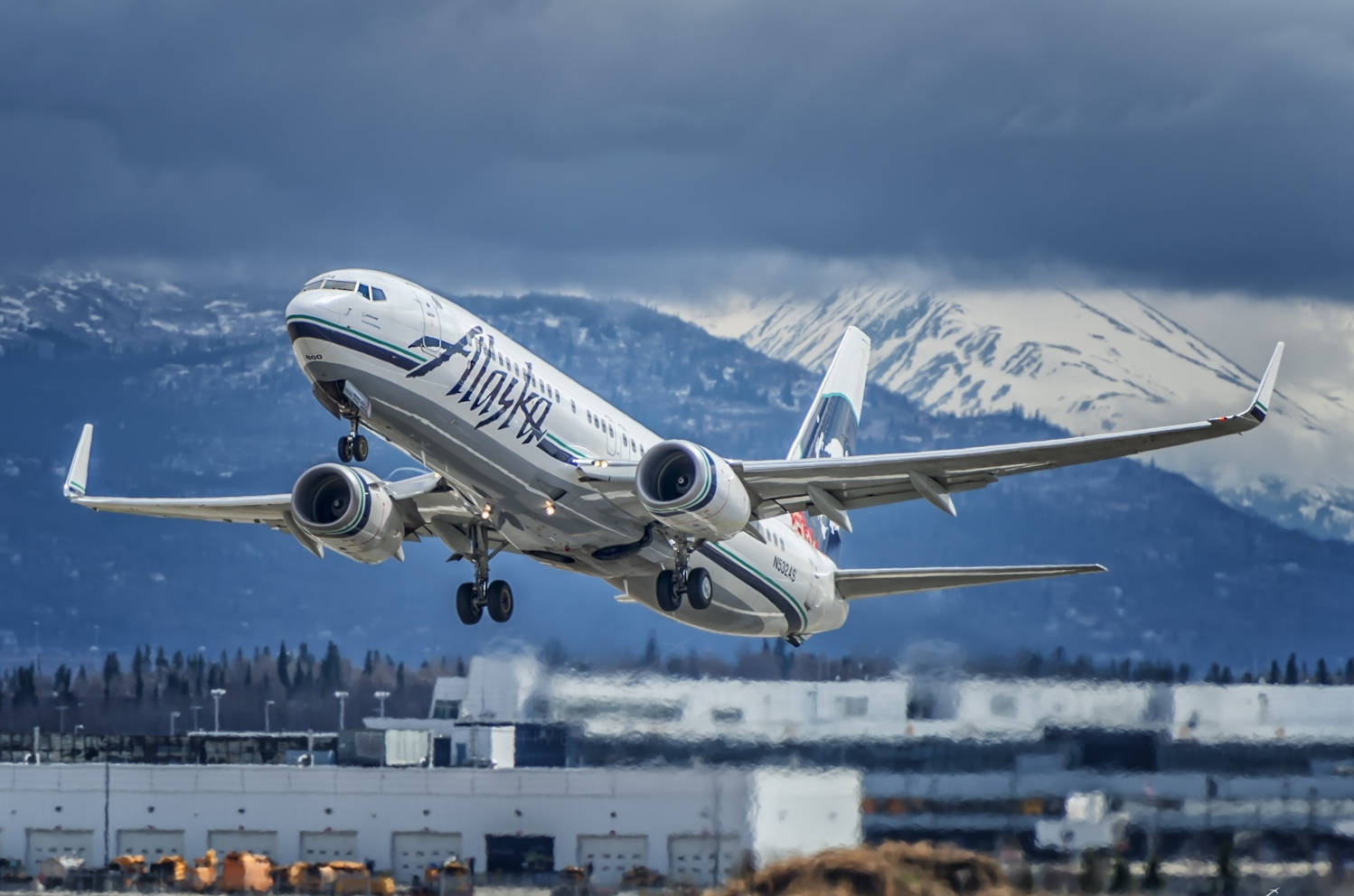 Plane 桌布 壁紙 — 阿拉斯加航空的飛機在戲劇性的多雲天空下，以積雪覆蓋的山脈為背景攀升。