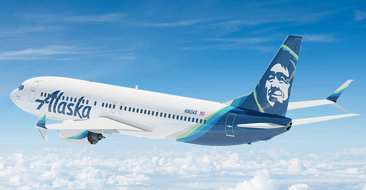 飛機 桌布 壁紙 — 阿拉斯加航空的飛機在晴朗的藍天下翱翔於蓬鬆的白雲之上，尾部帶有獨特的面部標誌。