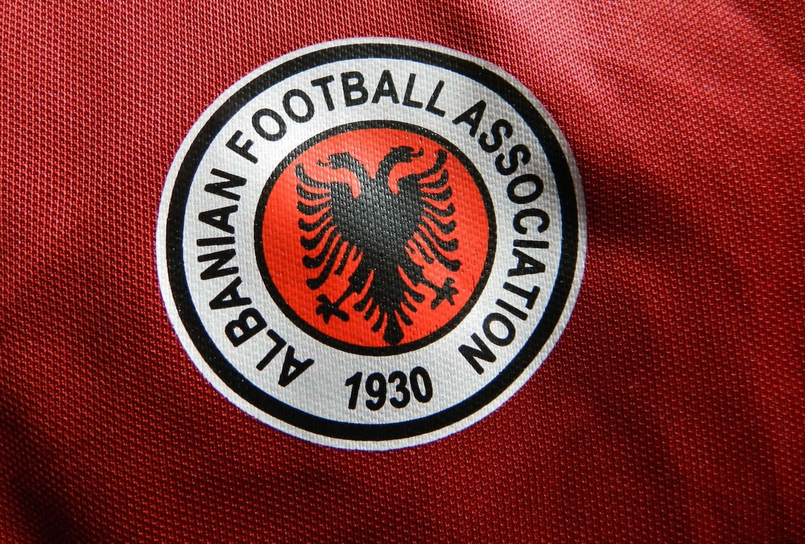 Albania 桌布 壁紙 — 阿爾巴尼亞足球協會徽章特寫，位於紅色紋理布料上，帶有黑色雙頭鷹和1930年日期。
