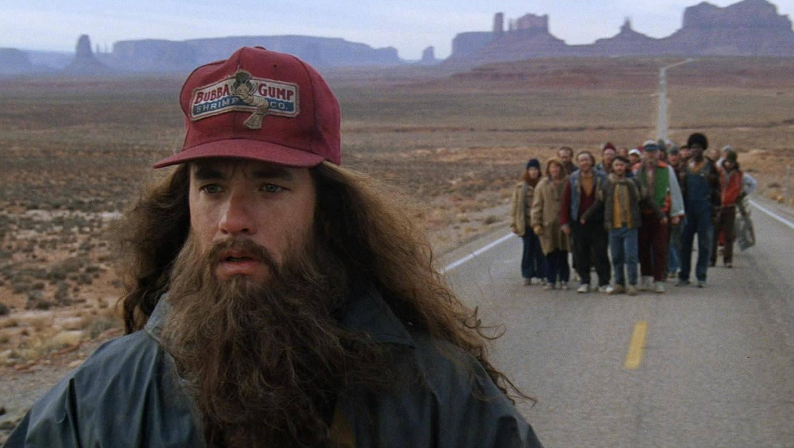 forrest 桌布 壁紙 — 阿甘在朦朧的天空下，沿著沙漠公路行走，身後跟著一群人。