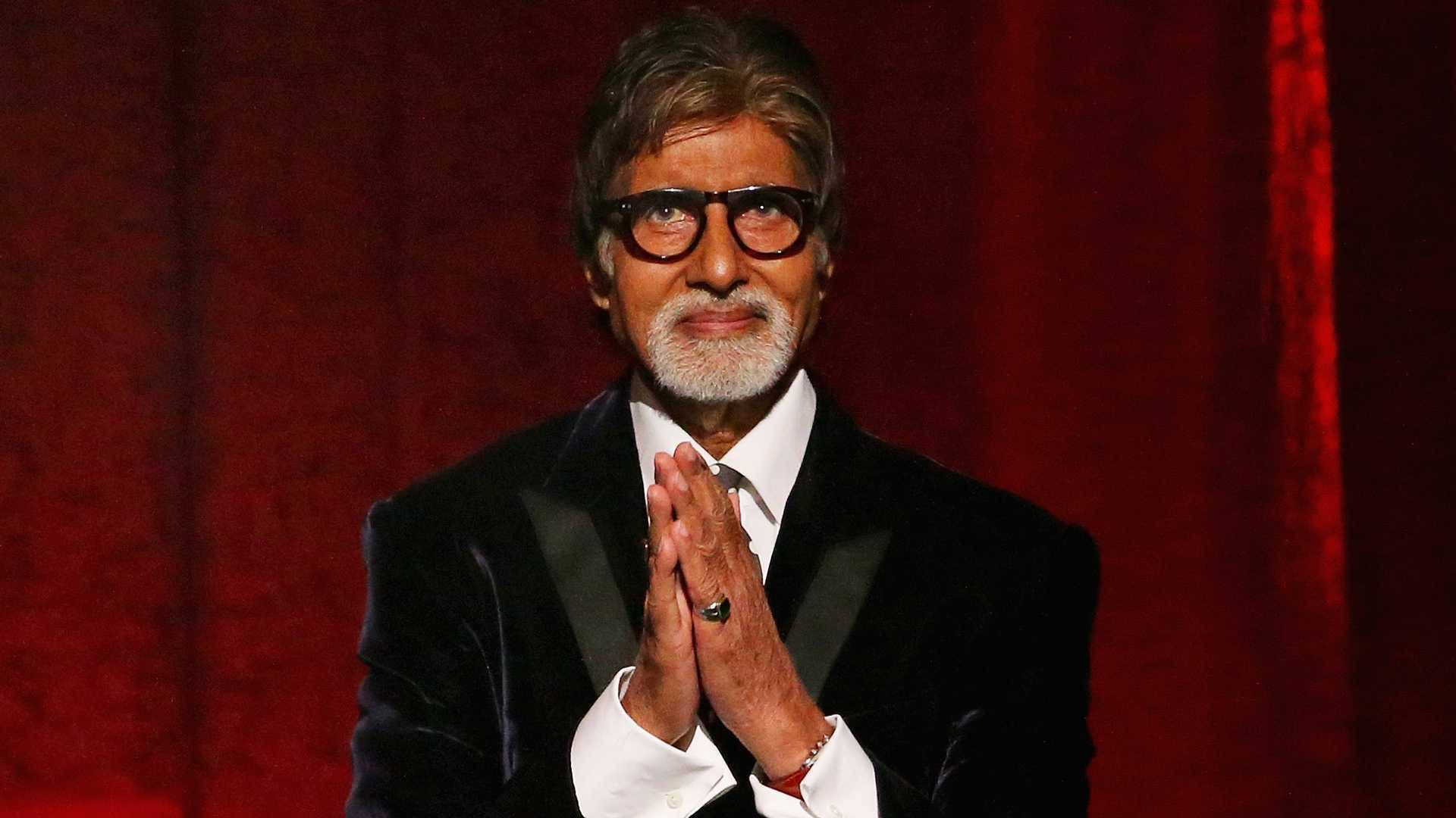 Amitabh Bachchan 桌布 壁紙 — 阿米塔布·巴強身穿黑色天鵝絨禮服，在深紅色帷幕背景下，雙手合十，做出恭敬的姿勢。